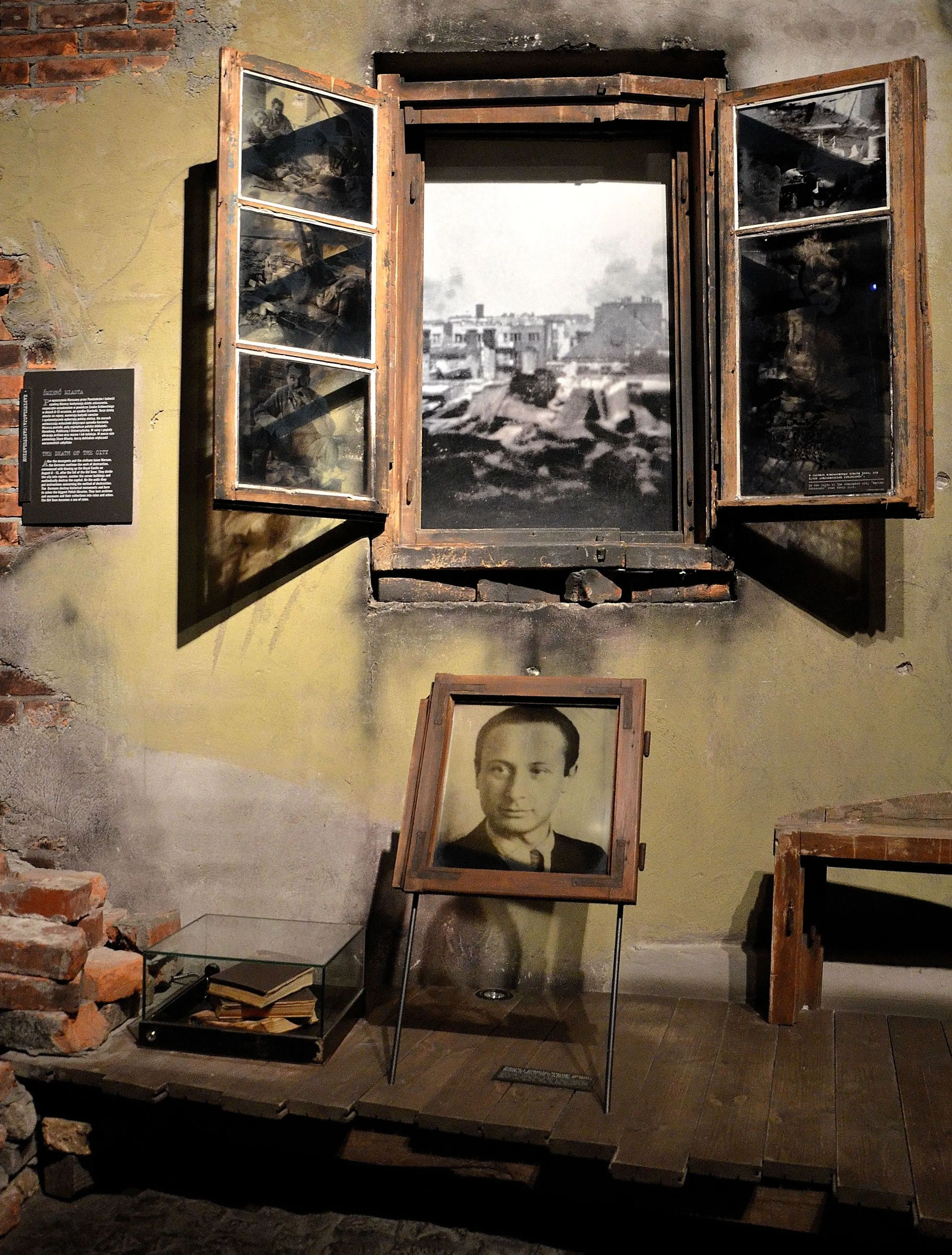 Een ingelijste portret van een man onder een groot raam met historische foto's, tentoongesteld in een museumexpositie met bakstenen muren en een vitrine.