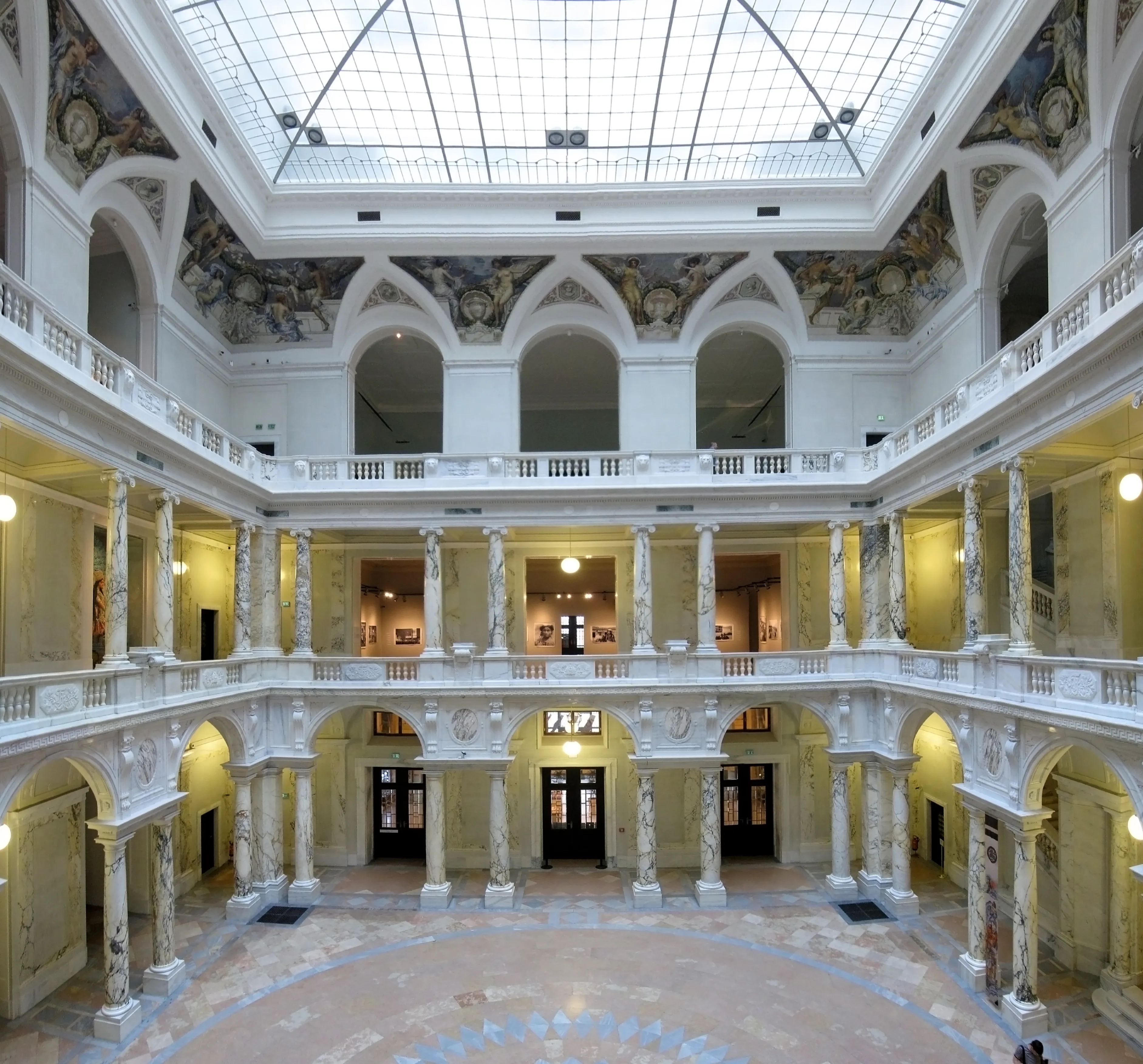 wielopoziomowe wnętrze z białymi kolumnami, łukowymi oknami i szklanym świetlikiem
