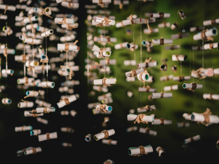 Hanging cylindrical paper objects suspended by strings in a dark interior space with green background