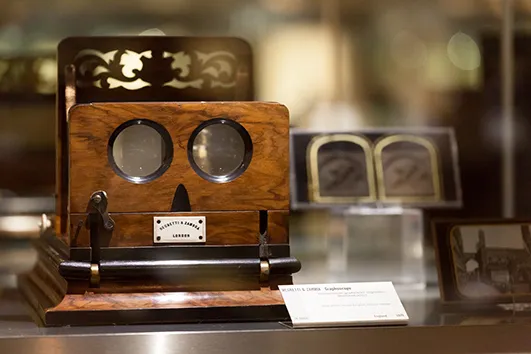 wooden stereoscopic camera with two lenses and a label on a display stand