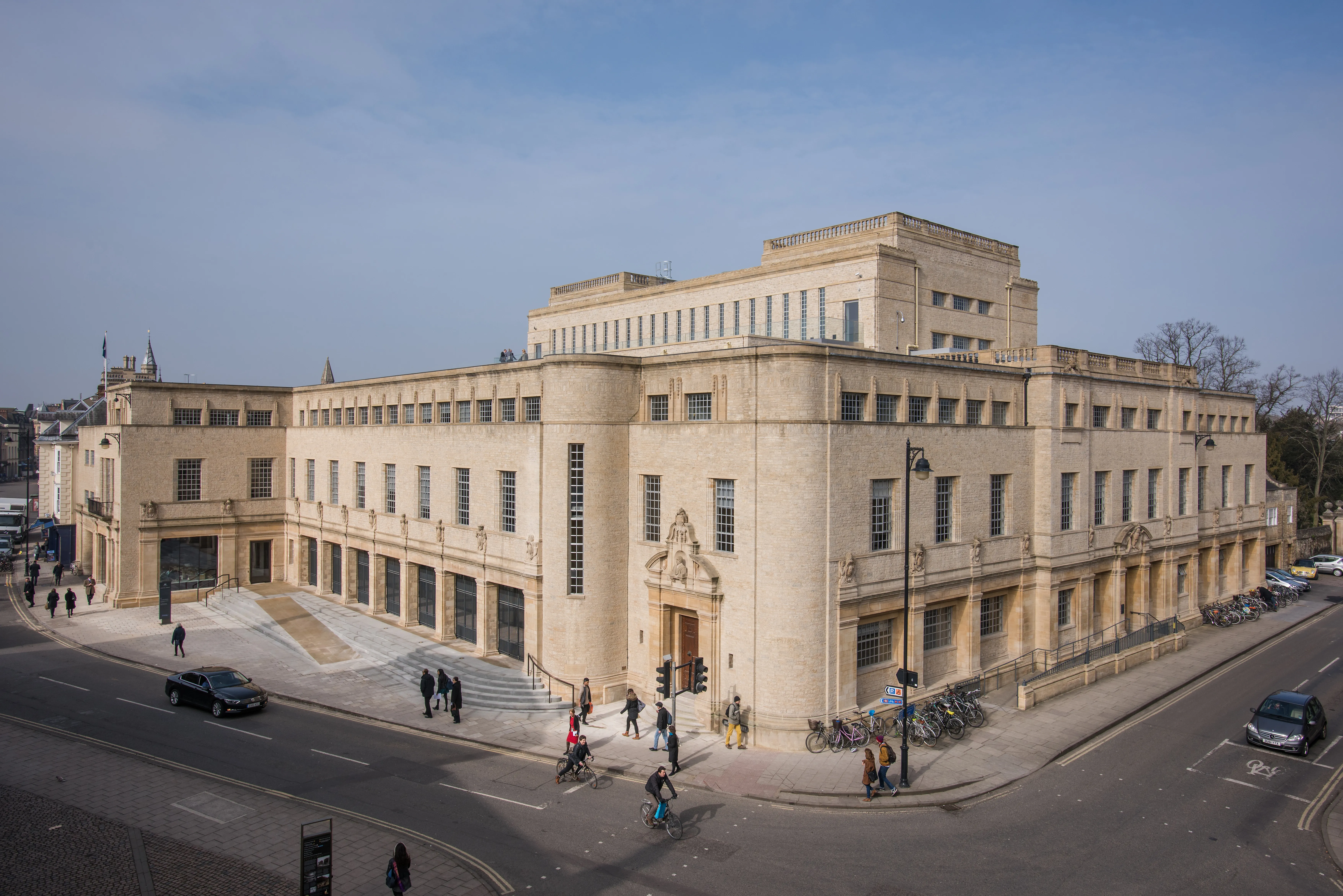 Exterior view of the Weston Library, a large light-stone Art Deco building on a street corner with pedestrians and cars.