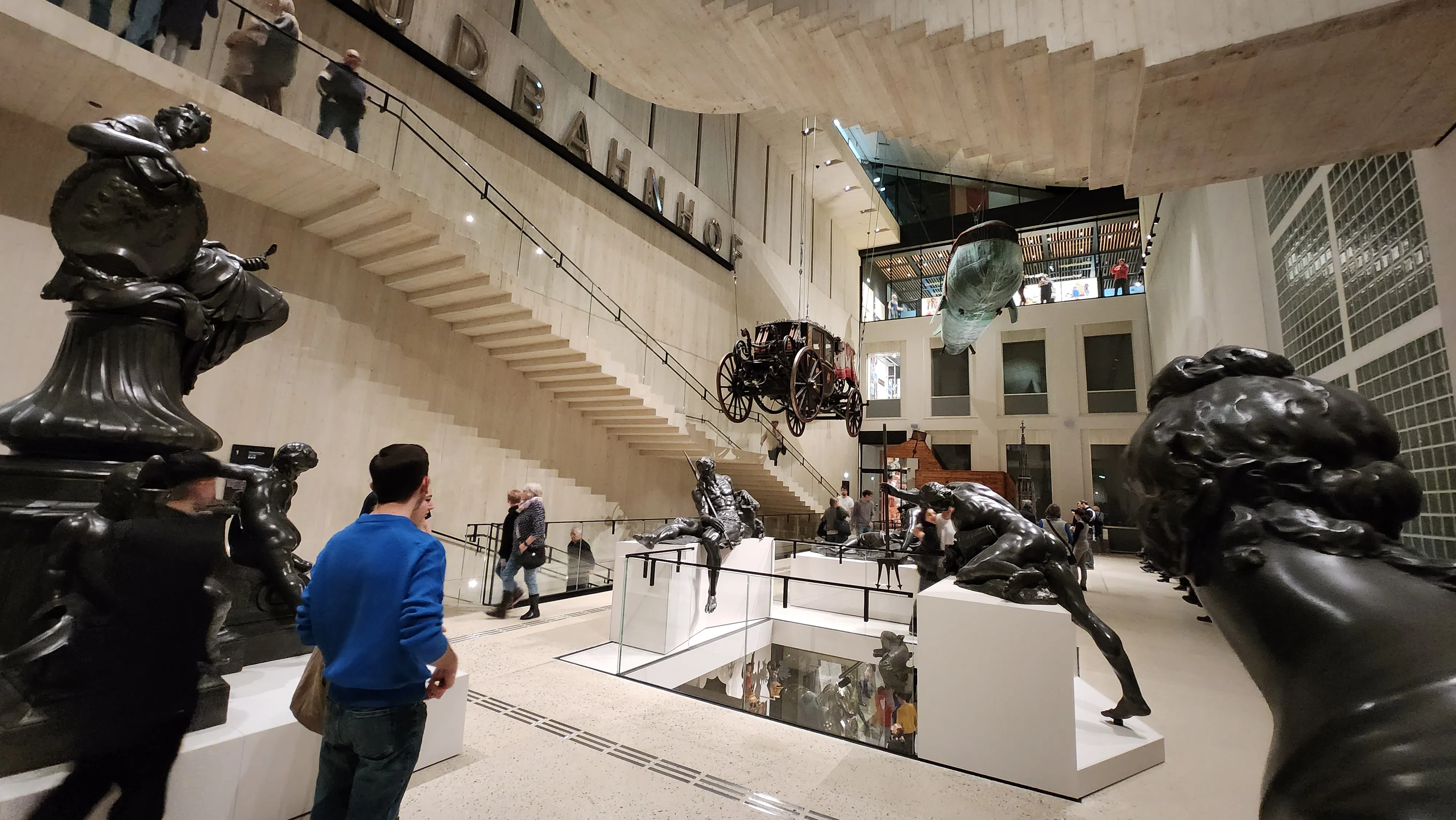 Interieur van het Wien Museum met sculpturen, een vintage auto en bezoekers