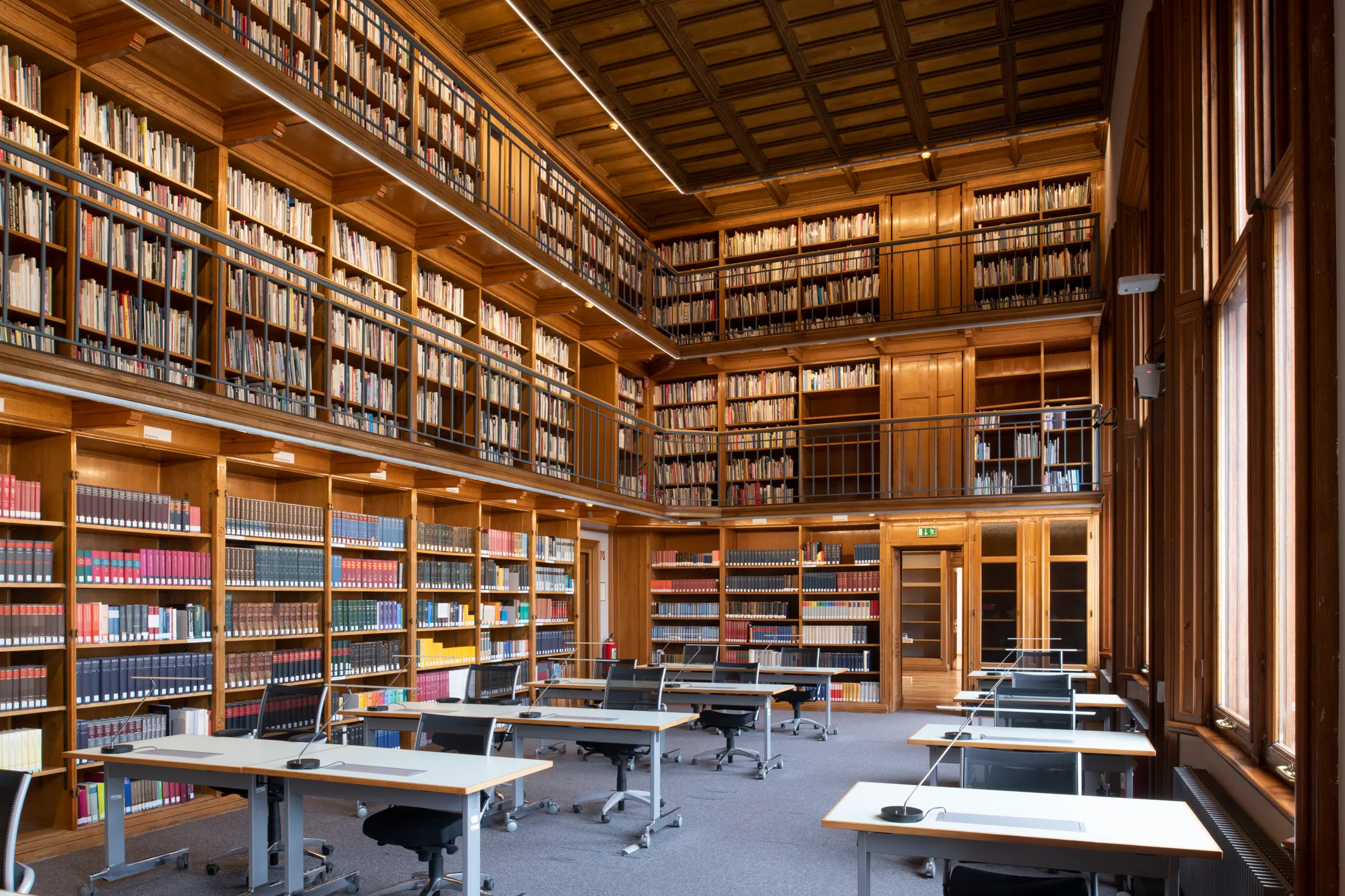 wnętrze biblioteki z wysokimi drewnianymi regałami, stołami do nauki i krzesłami