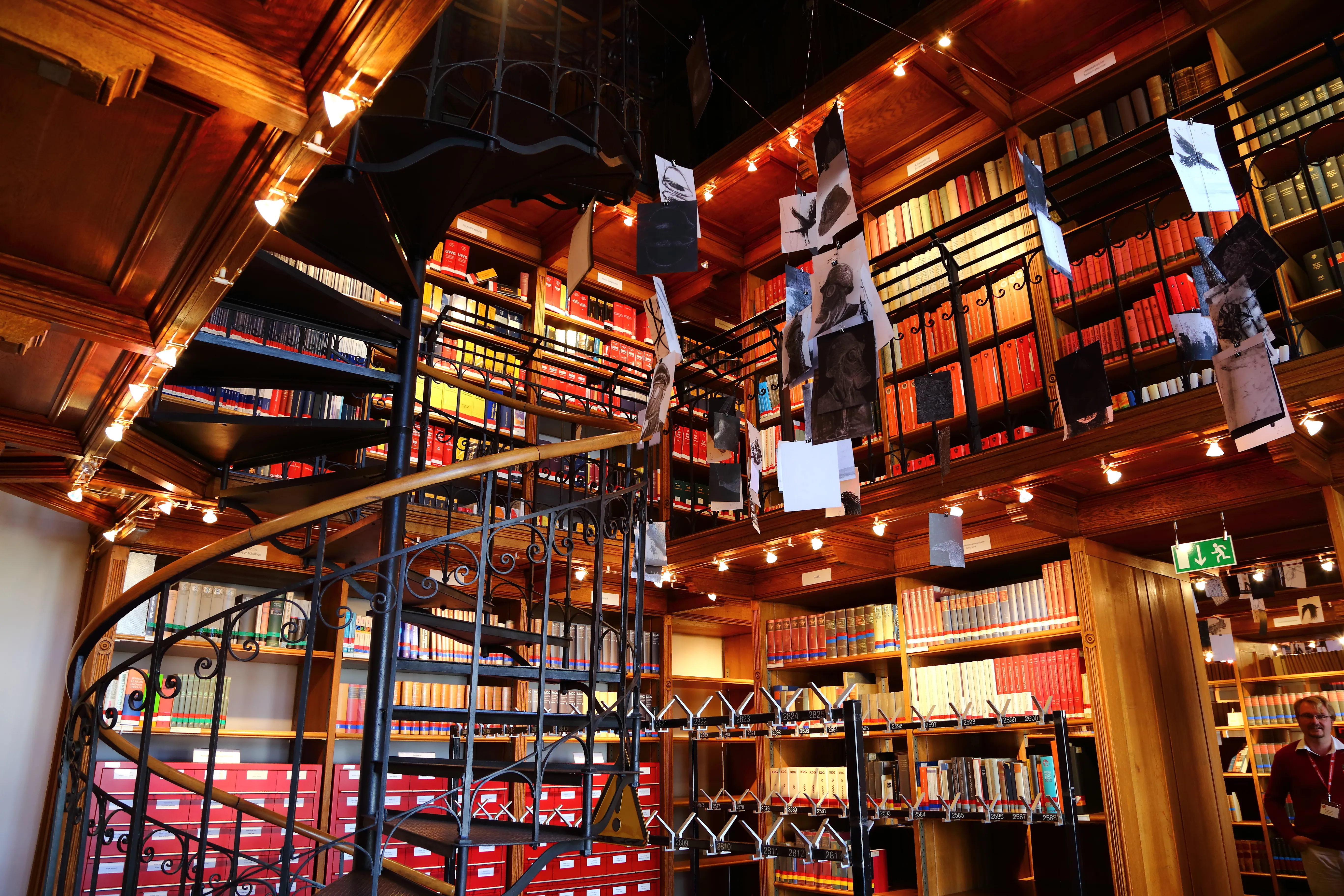 Wnętrze biblioteki ze spiralnymi schodami, drewnianymi regałami i wiszącymi wycinankami z papieru
