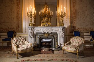 Elegant historic drawing room with ornate marble fireplace, gilded candelabras, patterned armchairs, and crystal chandelier at Museum Willet Holthuysen