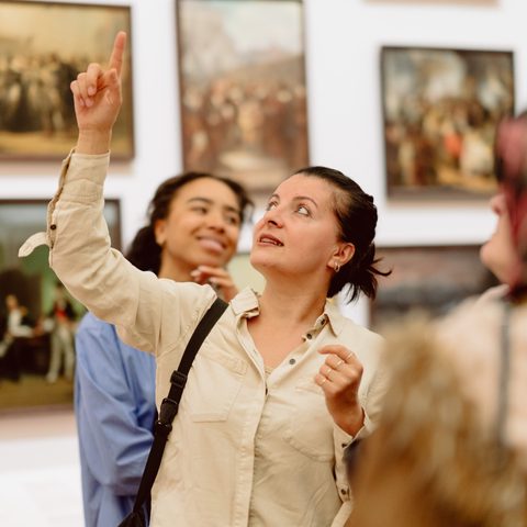 Visitors in a museum gallery looking at framed paintings on white walls, engaging with the exhibition