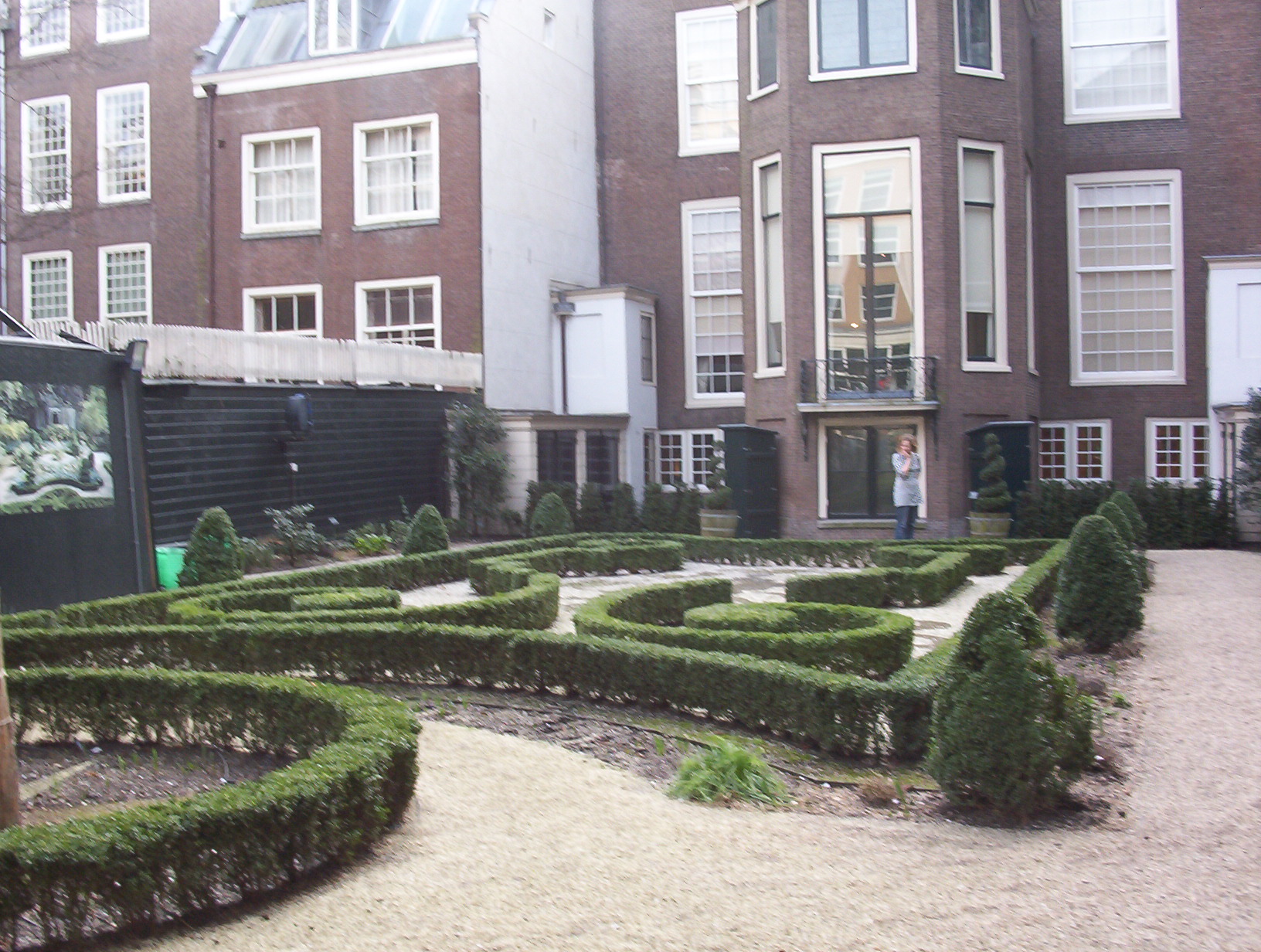 Brick canal house facade with symmetrical windows and a formal garden featuring geometric hedge mazes and gravel paths