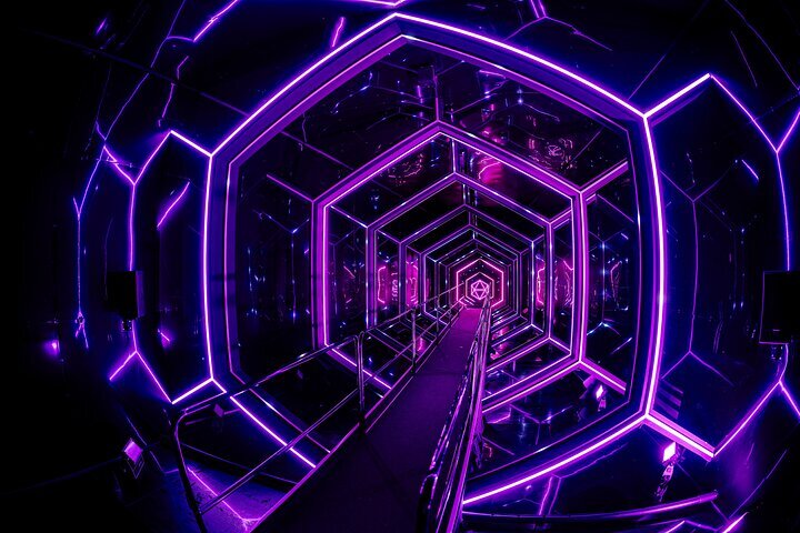 A vibrant purple neon-lit hexagonal tunnel installation with a central walkway, part of the WONDR Experience's interactive exhibition.