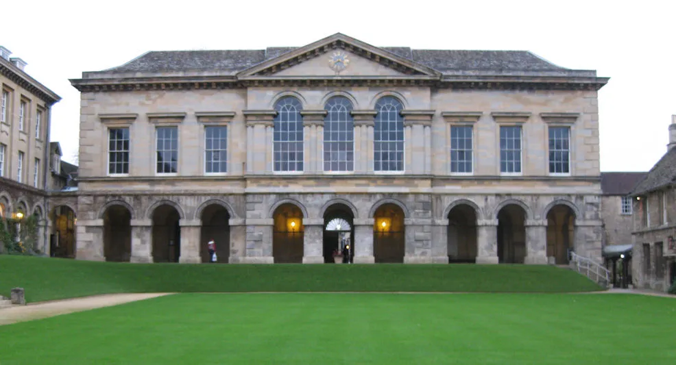 Klasyczny kamienny budynek z arkadową kolumnadą i dużymi oknami, widoczny przez zielony trawnik na dziedzińcu Worcester College
