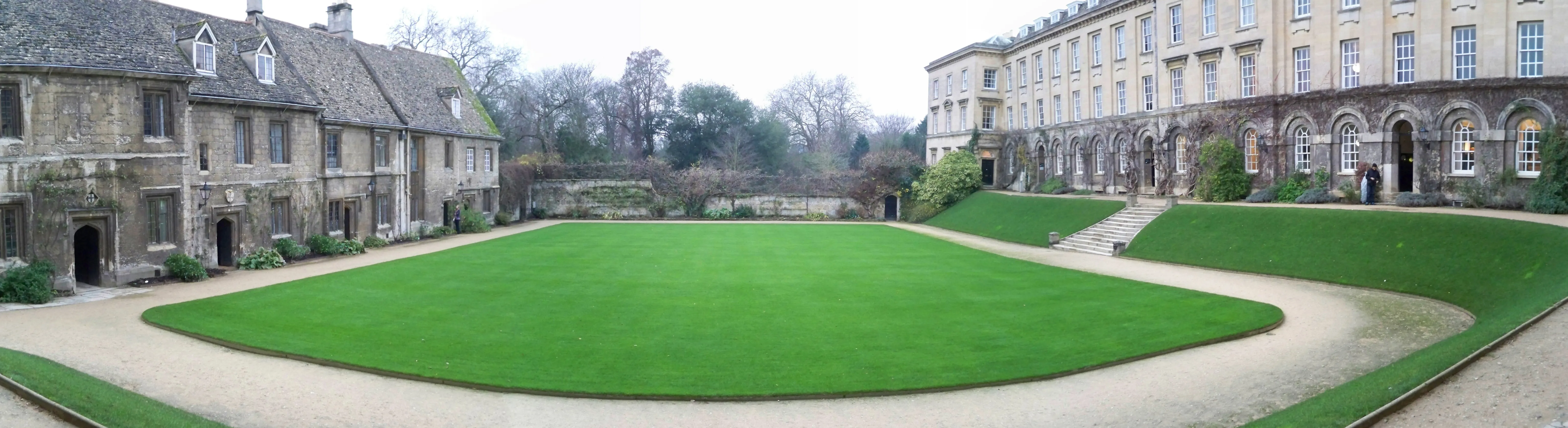 Szeroki panoramiczny widok na dziedziniec Worcester College z dużym owalnym trawnikiem otoczonym żwirowymi ścieżkami oraz zabytkowymi kamiennymi budynkami po obu stronach
