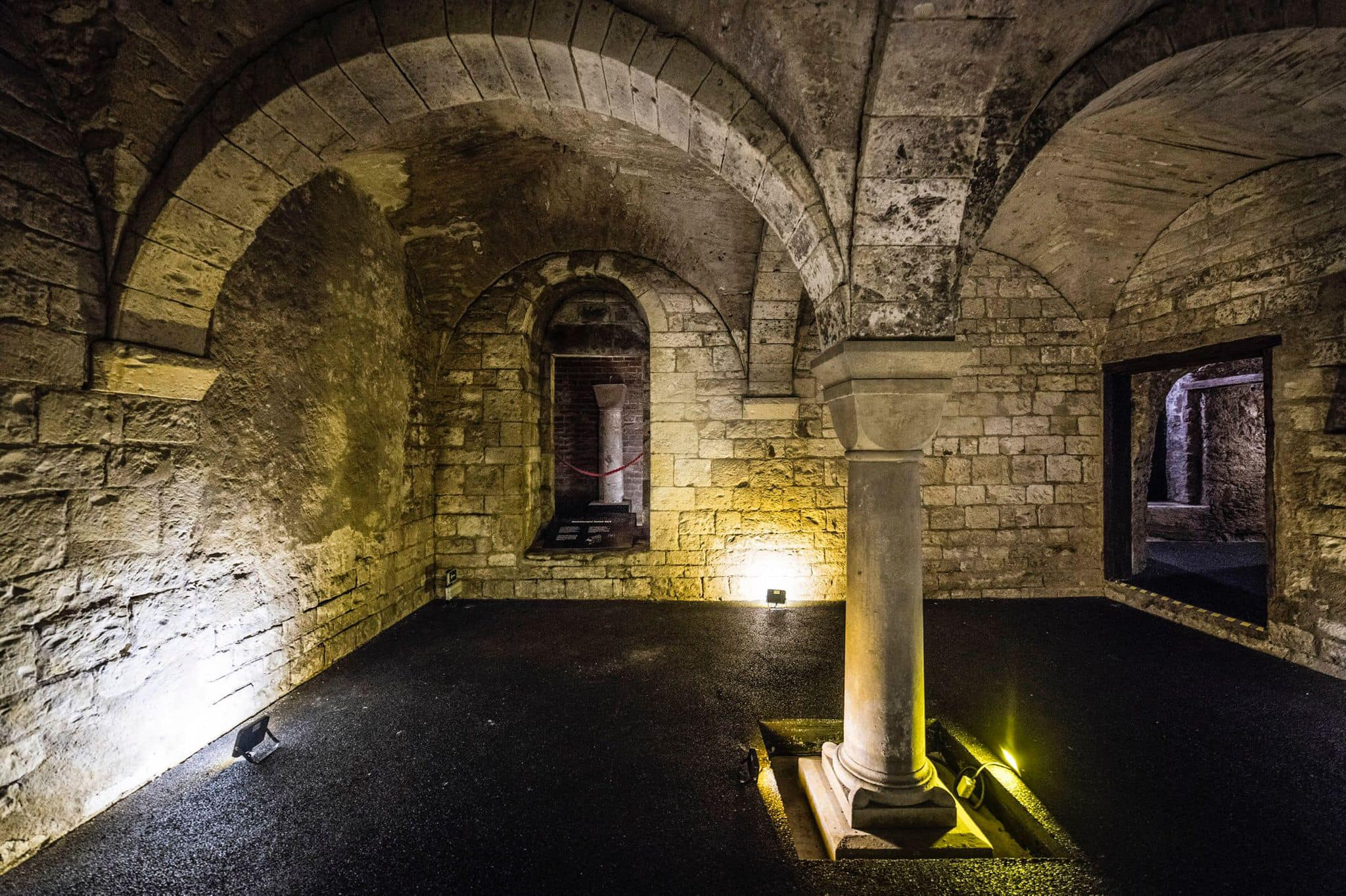 Stone vaulted ceiling and arched walls in a dimly lit interior space with a central column and warm lighting