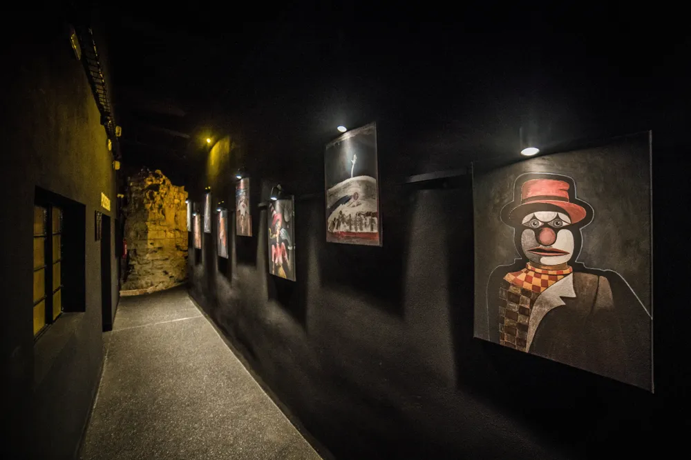 Dark hallway with framed artworks on the walls, including a painting of a clown in a red hat
