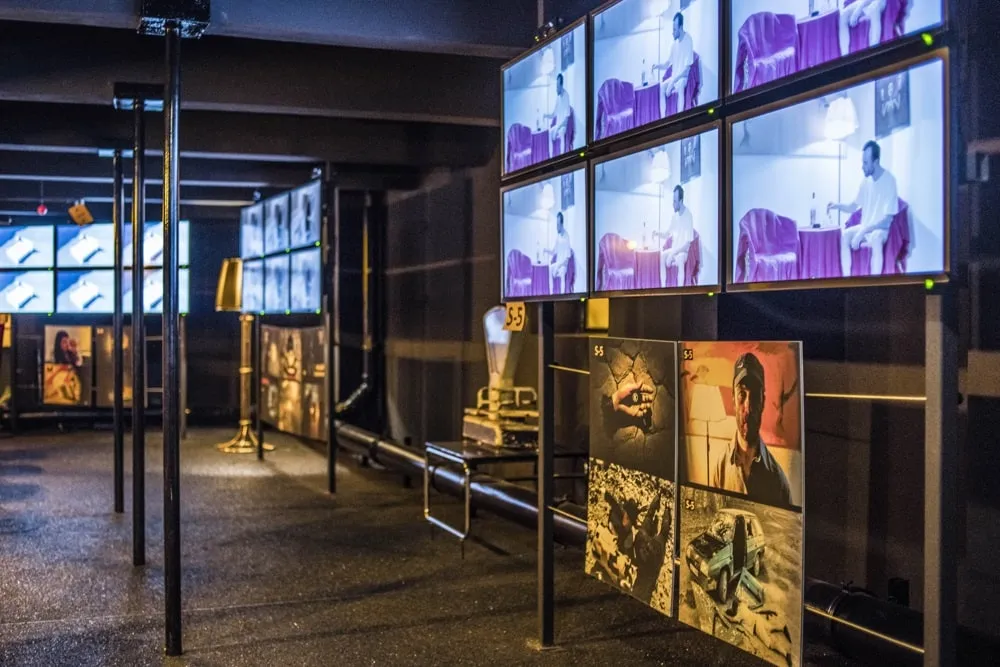 Multiple screens displaying surreal projections in a dark room with artwork panels below