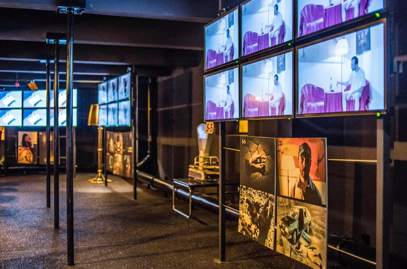 A dark gallery with multiple screens showing surreal images and a display of artwork on the wall.