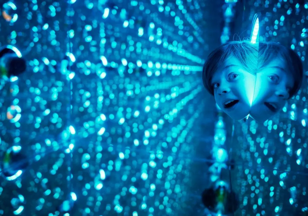A person's face reflected in a mirrored room with blue lights creating a tunnel effect