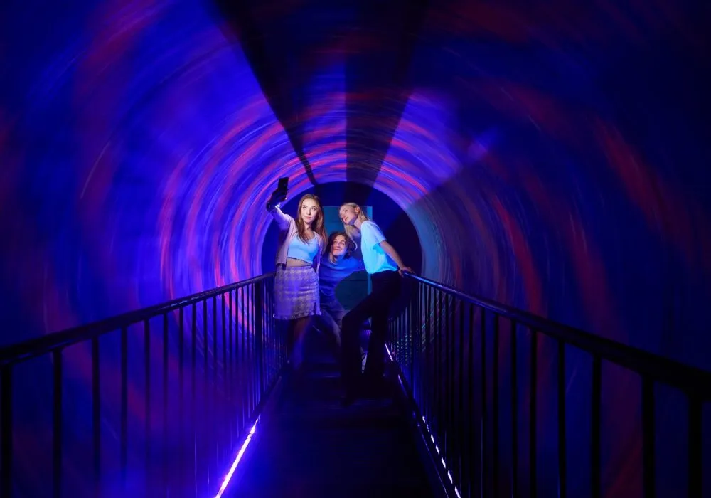 Three people standing in a tunnel with swirling blue and red lights creating an optical illusion effect