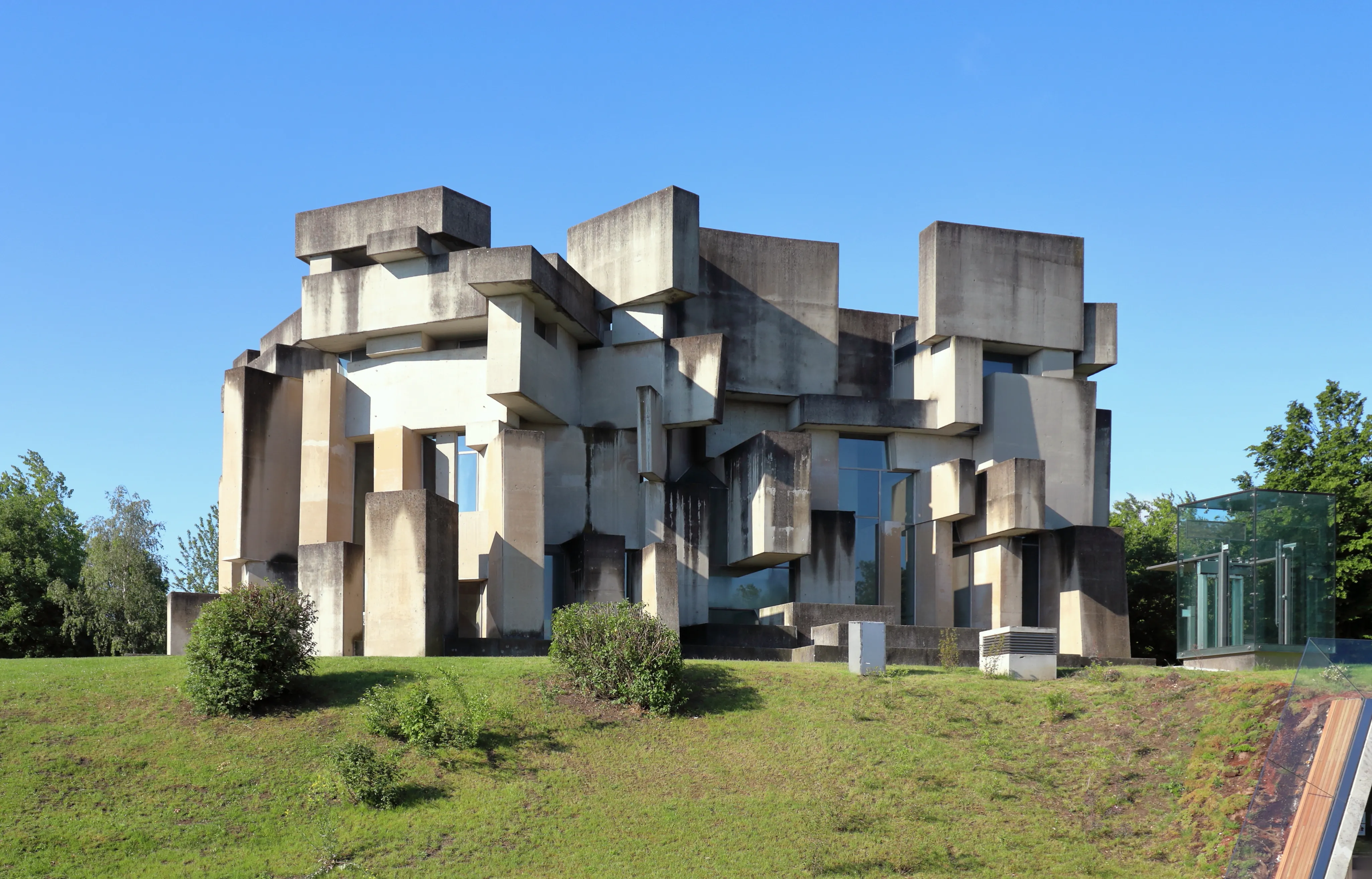 Modern betonnen kerkgebouw met geometrische gestapelde blokken, groen gras en blauwe lucht