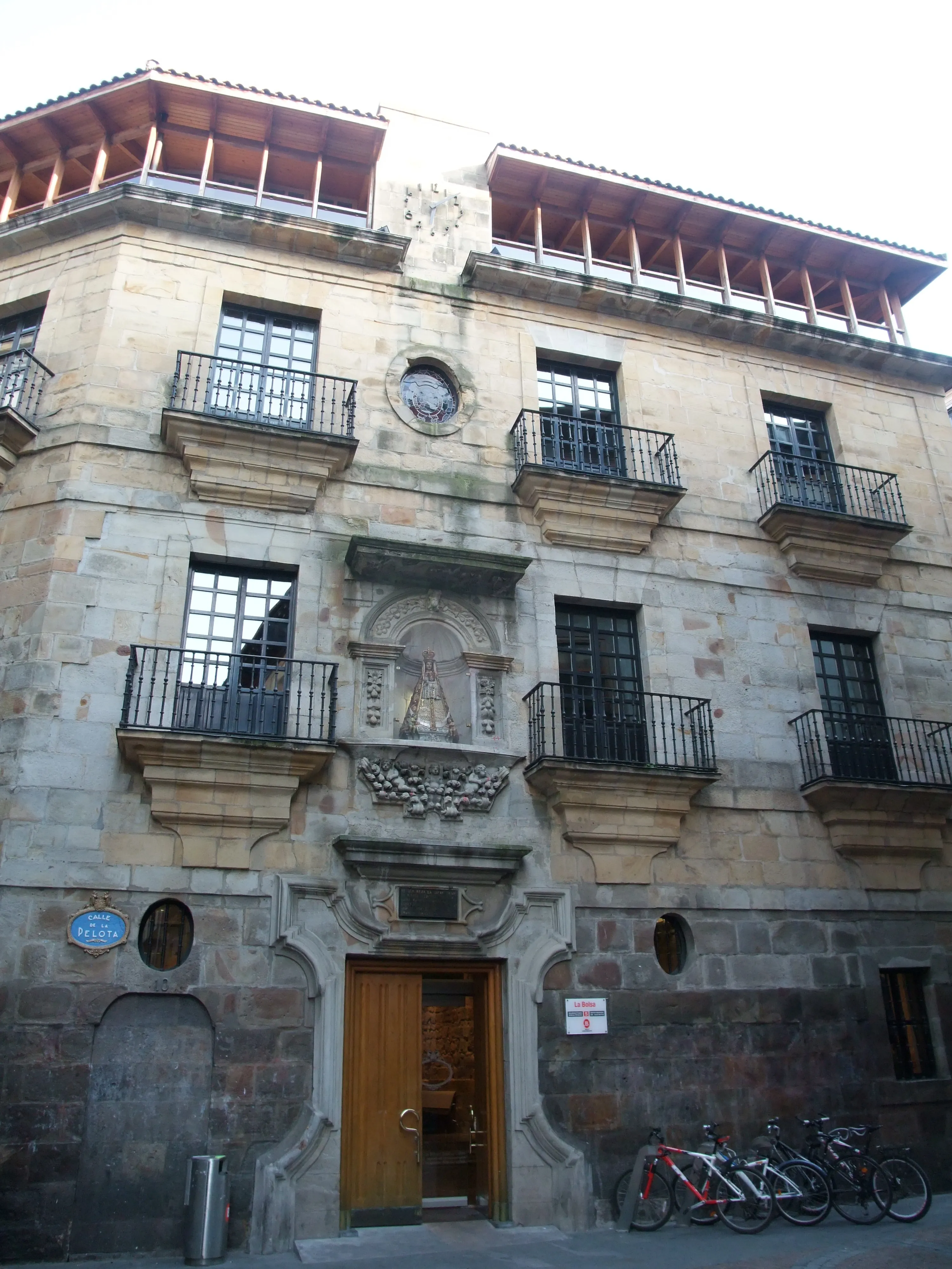 Stone facade of a historic Baroque palace with wrought-iron balconies, a central arched doorway, and bicycles parked along the street.