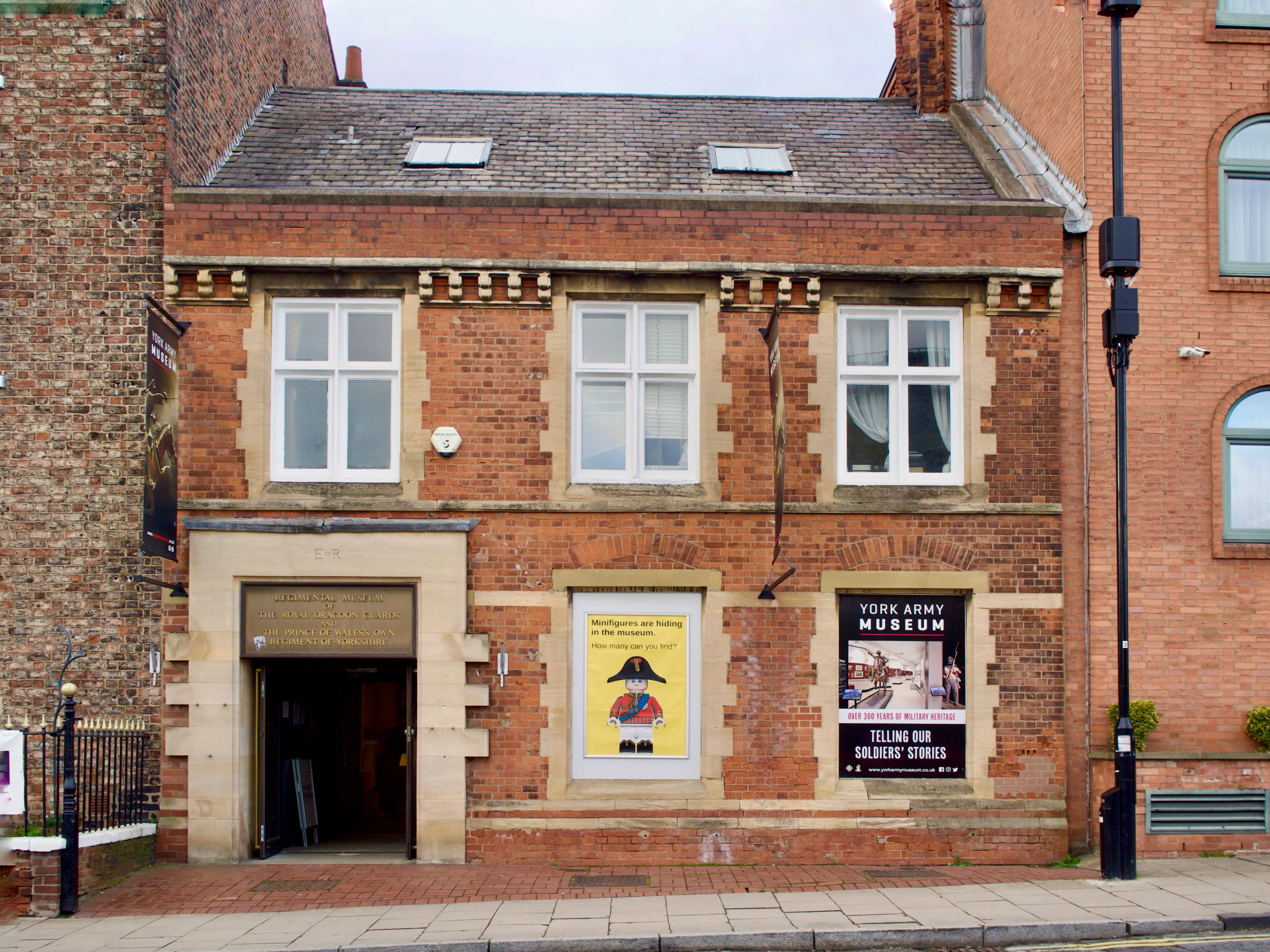Fachada de ladrillo del York Army Museum con entrada enmarcada en piedra, ventanas en la planta superior y un letrero negro que dice 'York Army Museum - Telling Our Regiment's Stories'