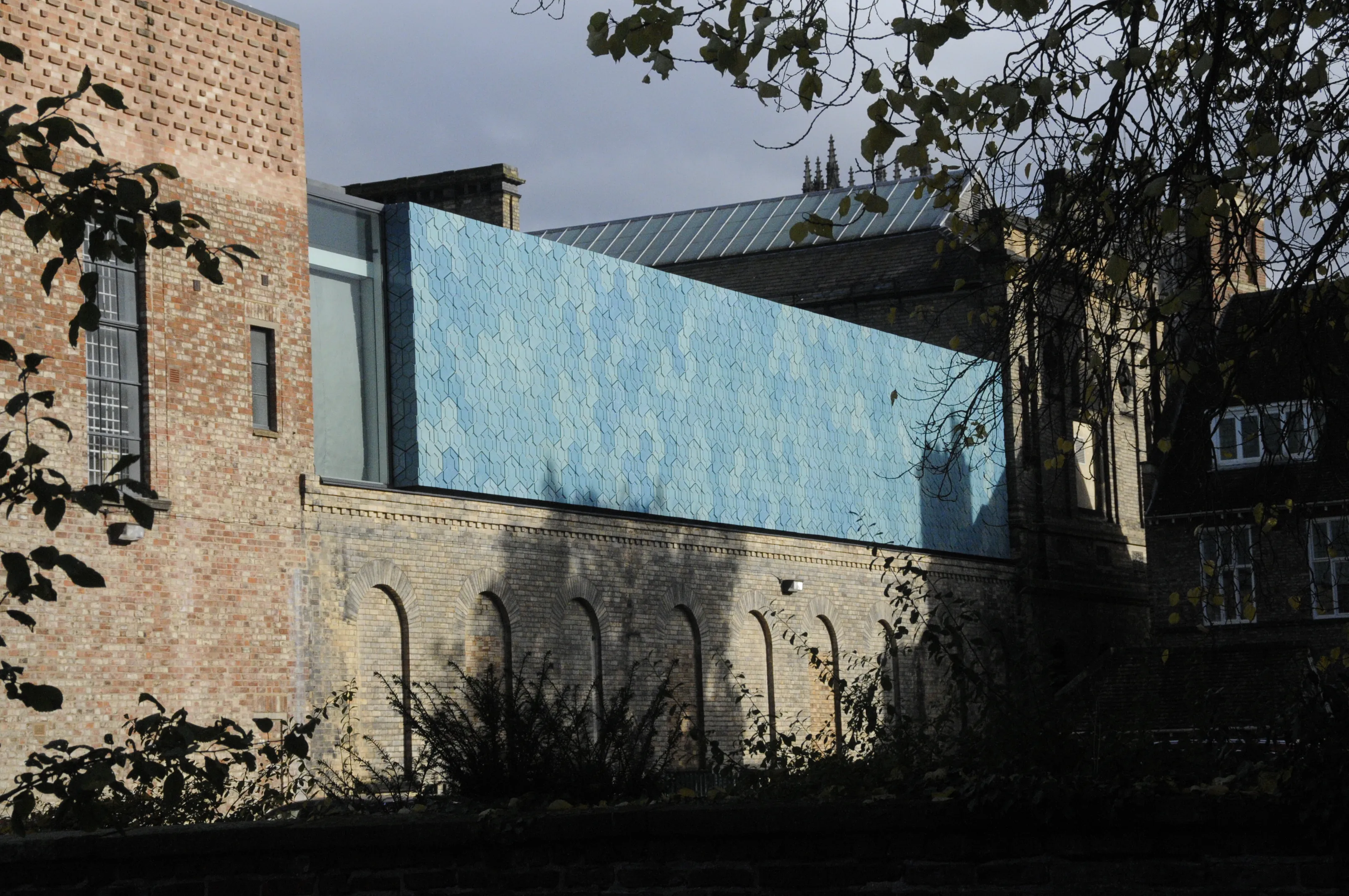 Widok z zewnątrz York Art Gallery przedstawiający nowoczesną, wyłożoną niebieskimi płytkami rozbudowę przylegającą do zabytkowego ceglanego budynku, w otoczeniu drzew