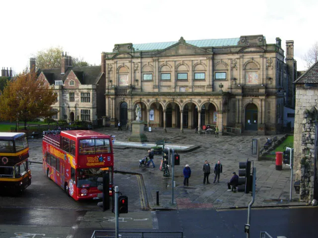 Kamienna fasada York Art Gallery z łukowatymi oknami i wejściami, widziana z placu Exhibition Square z czerwonymi autobusami piętrowymi i pieszymi na pierwszym planie.
