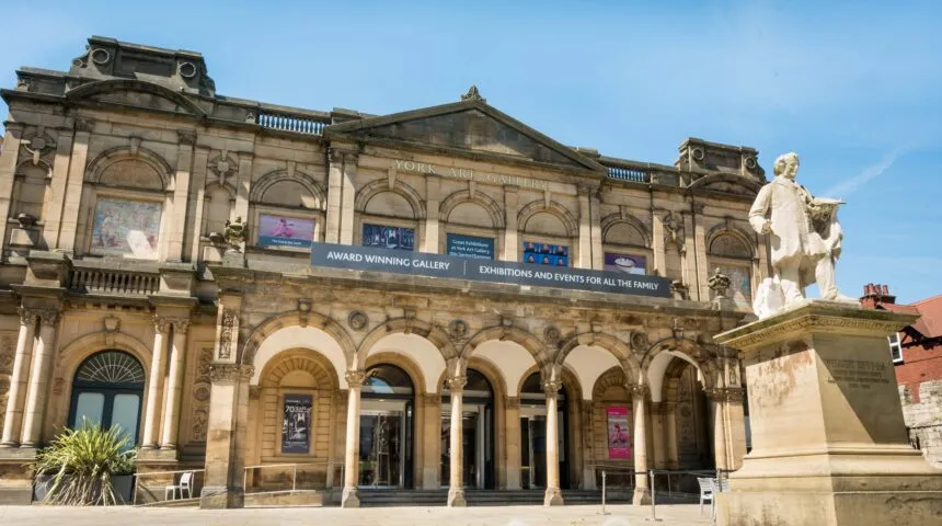 Fasada York Art Gallery prezentująca klasyczną kamienną elewację z łukowymi kolumnadami, dużymi oknami oraz białą rzeźbą na cokole na pierwszym planie