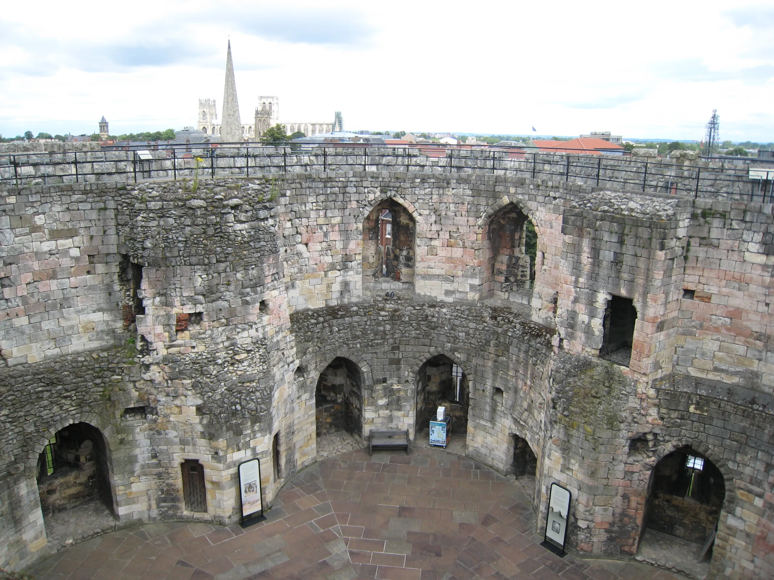 Vista interior de Clifford's Tower que muestra paredes circulares de piedra con aberturas arqueadas y la aguja de York Minster visible al fondo
