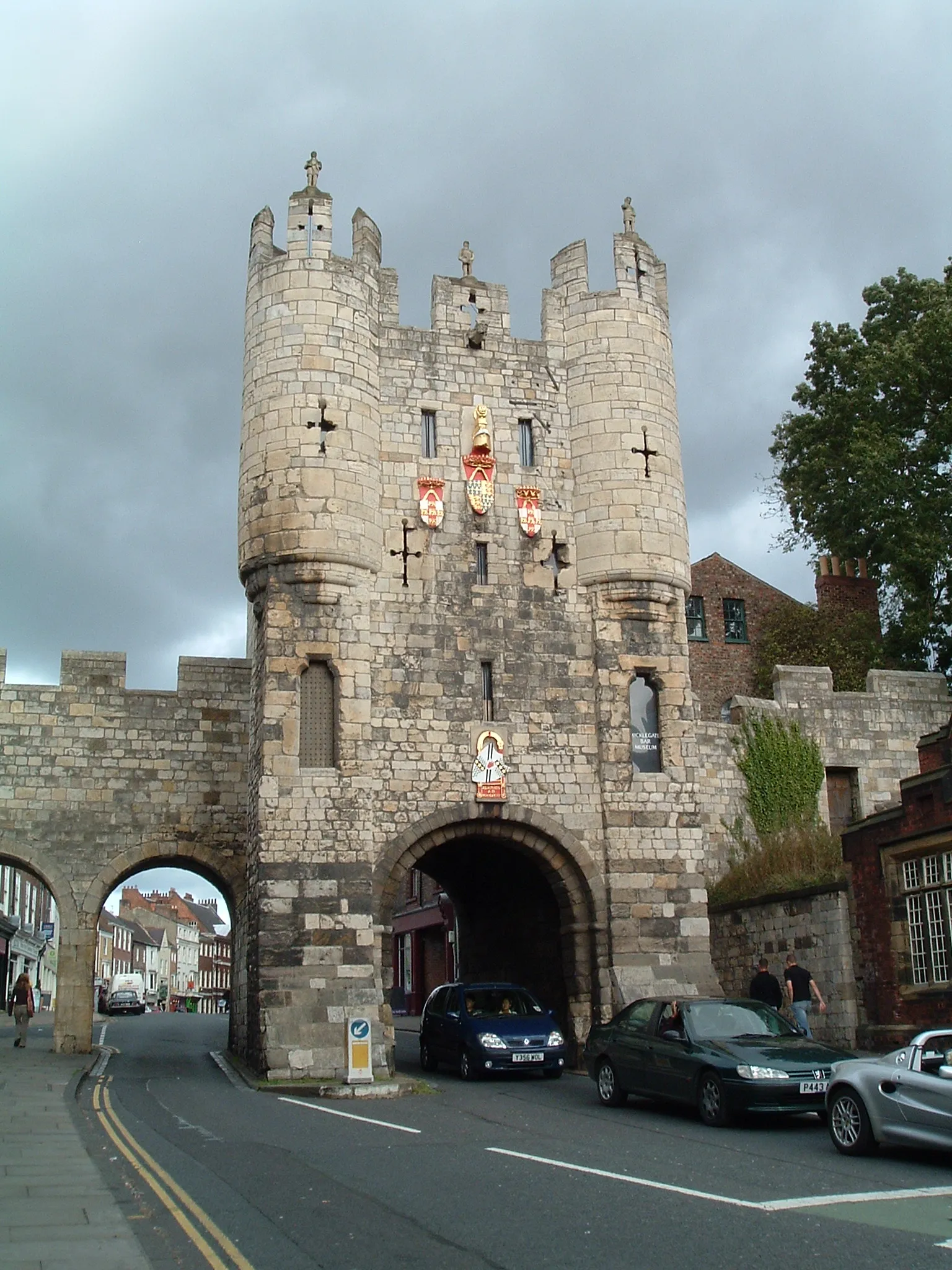 Casa de guardia medieval de piedra con dos arcos, uno para peatones y otro para vehículos, que presenta escudos de armas en la fachada.