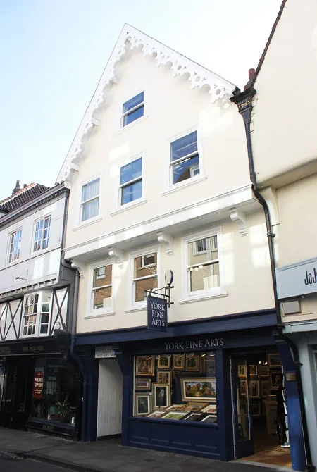 Edificio blanco de tres plantas con hastial y escaparate azul que exhibe cuadros enmarcados, con el letrero de York Fine Arts colgado sobre la entrada