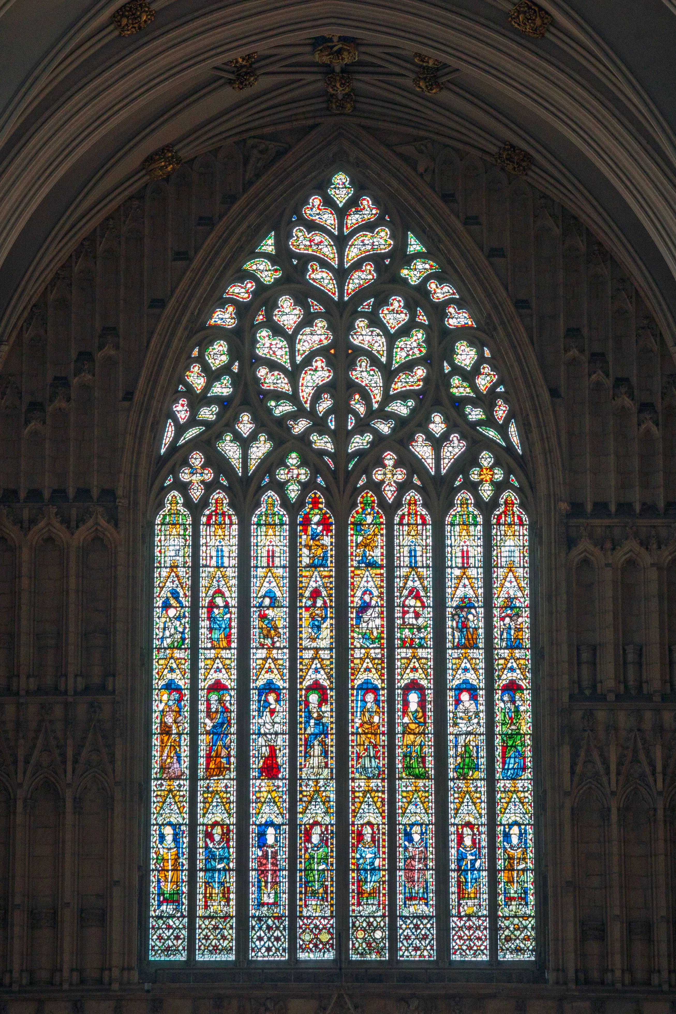 Tall Gothic stained glass window with intricate stone tracery and colorful panels depicting figures, set within a stone archway inside York Minster.