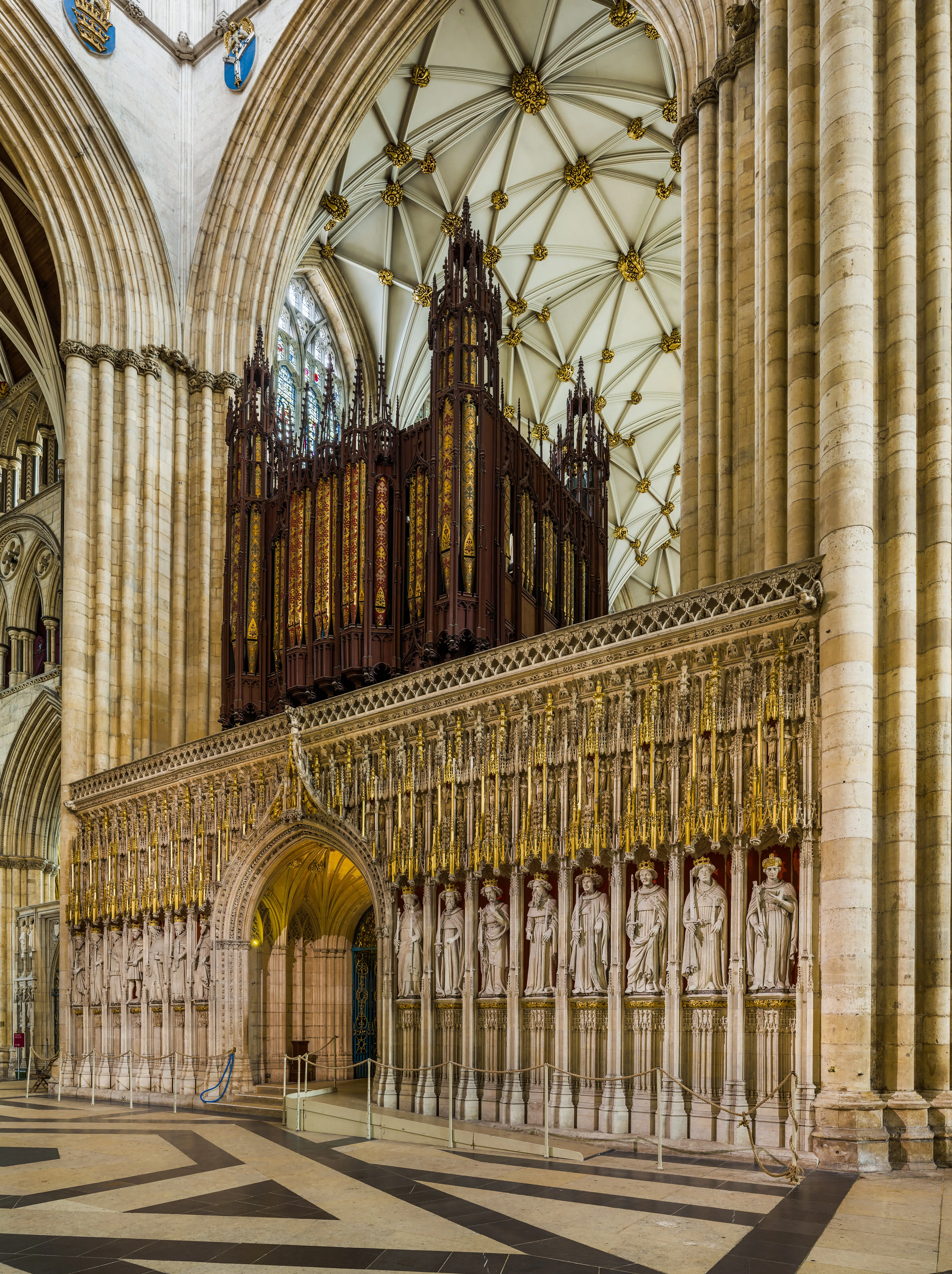 Ornate stone rood screen with carved royal statues and gilded tracery inside York Minster, with pipe organ and fan-vaulted ceiling above