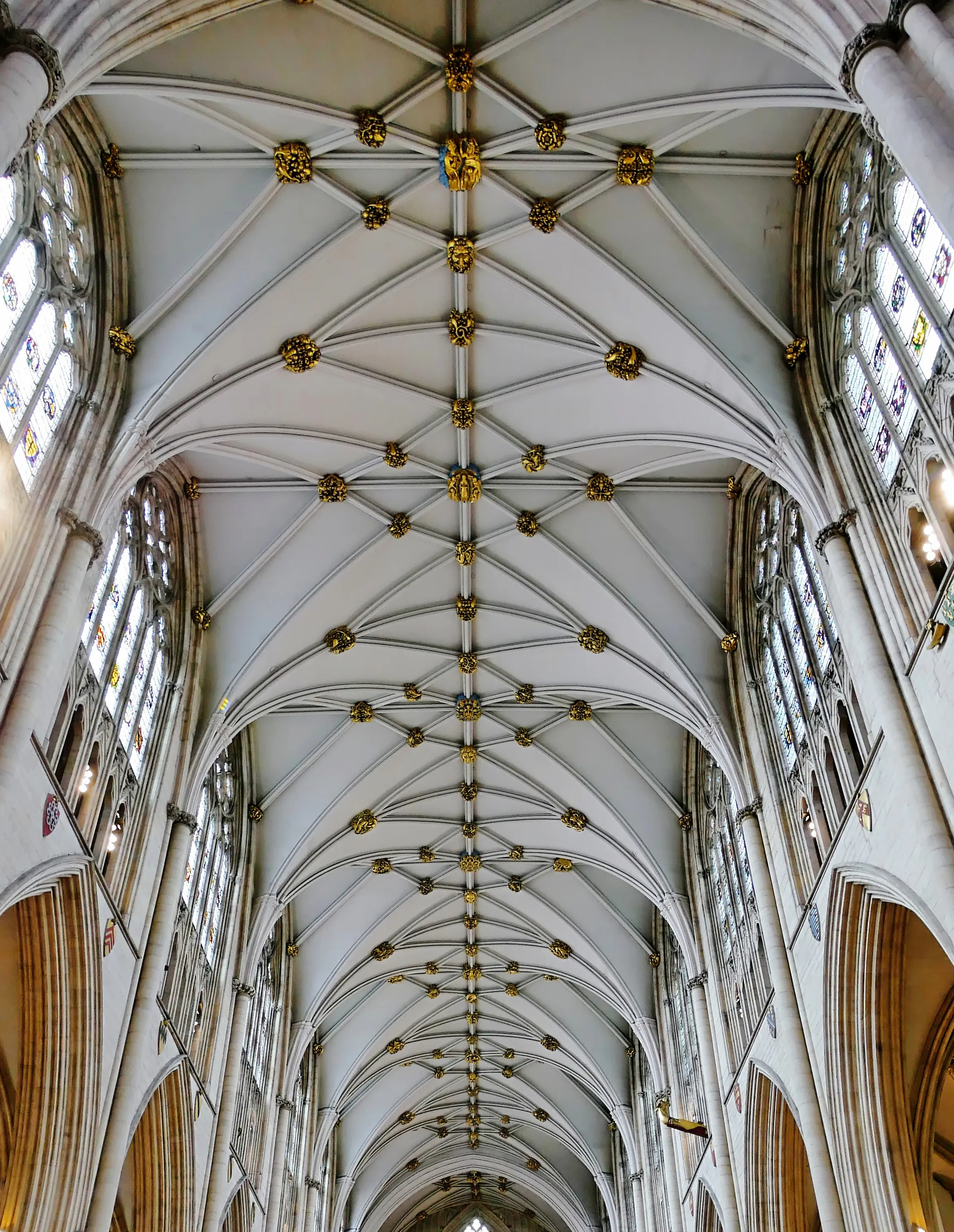 Vaulted stone ceiling of York Minster nave with golden bosses and clerestory stained glass windows