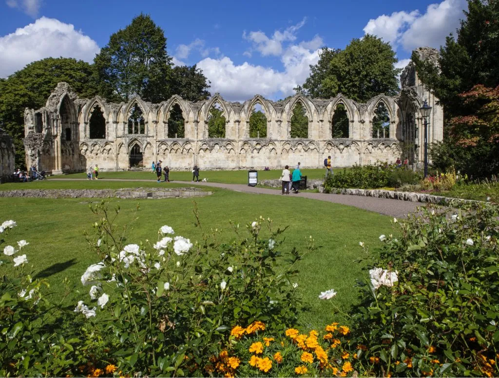 Ruinas de una abadía de piedra medieval con altos ventanales de arco gótico situadas detrás de un césped verde y parterres en los York Museum Gardens