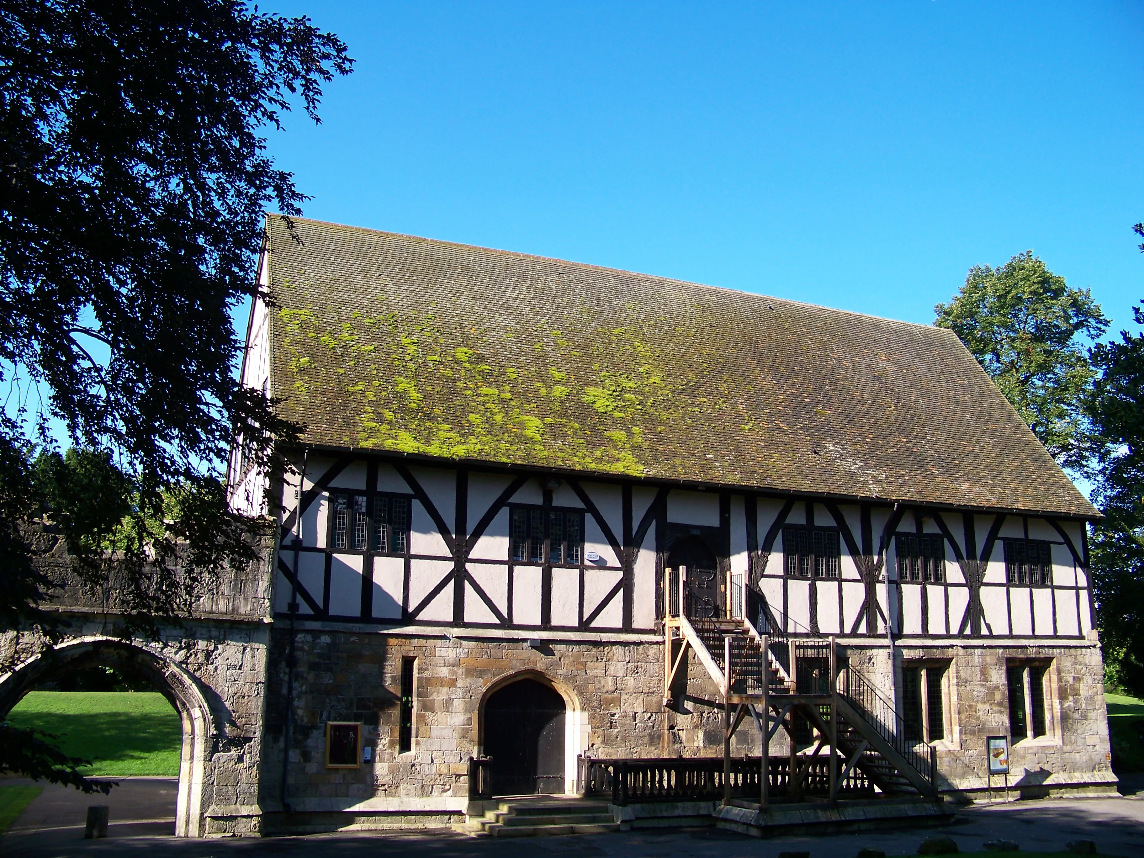 Vista exterior del Hospitium, un histórico edificio de entramado de madera con base de piedra, tejado cubierto de musgo y una escalera exterior de madera en los York Museum Gardens.
