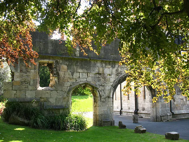 Ruinas de piedra con aberturas arqueadas rodeadas de árboles verdes y césped en los York Museum Gardens.