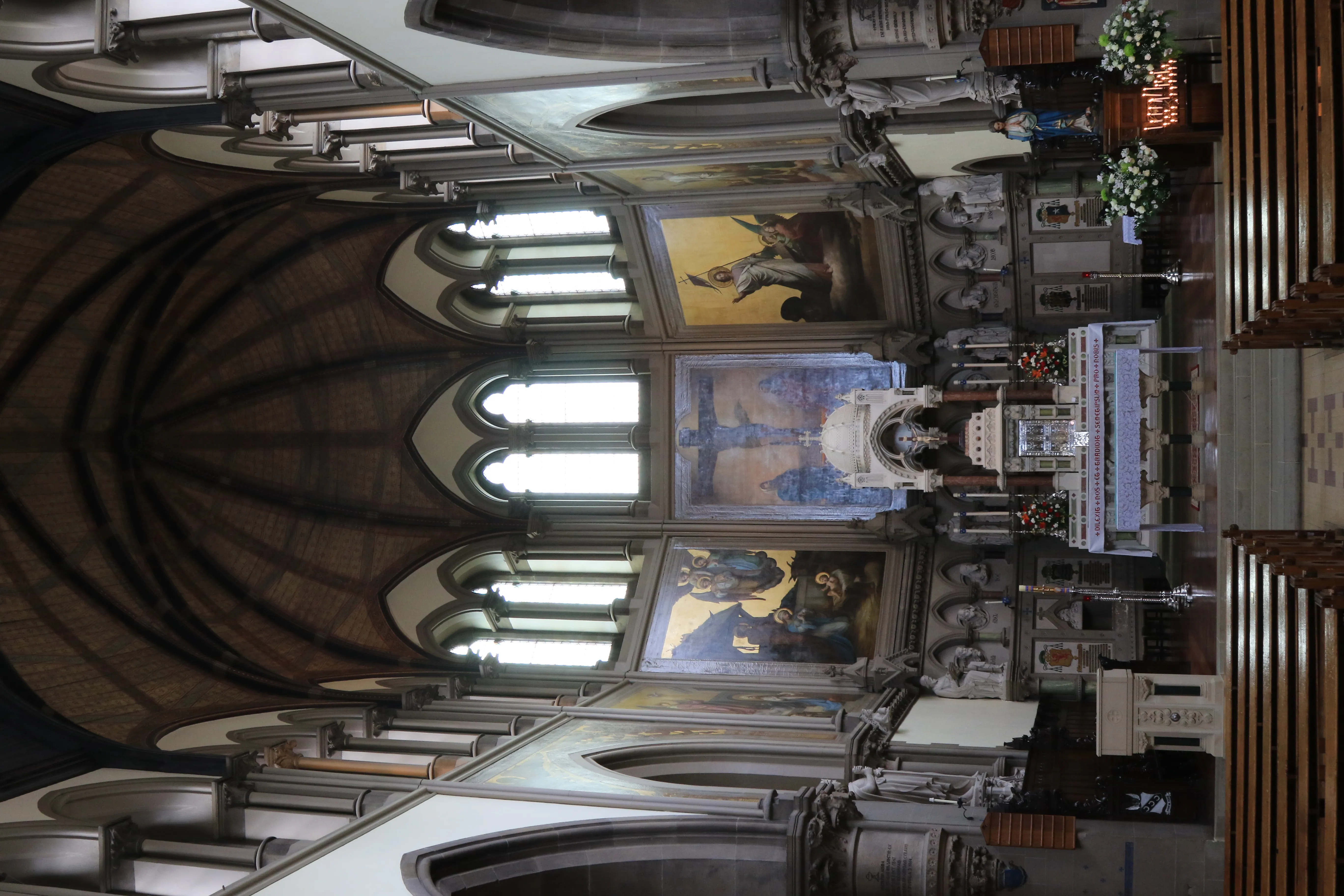 Interior of St Wilfrid's Church showing the nave and chancel with vaulted ceiling, tall arched windows, wooden pews, high altar, and religious murals