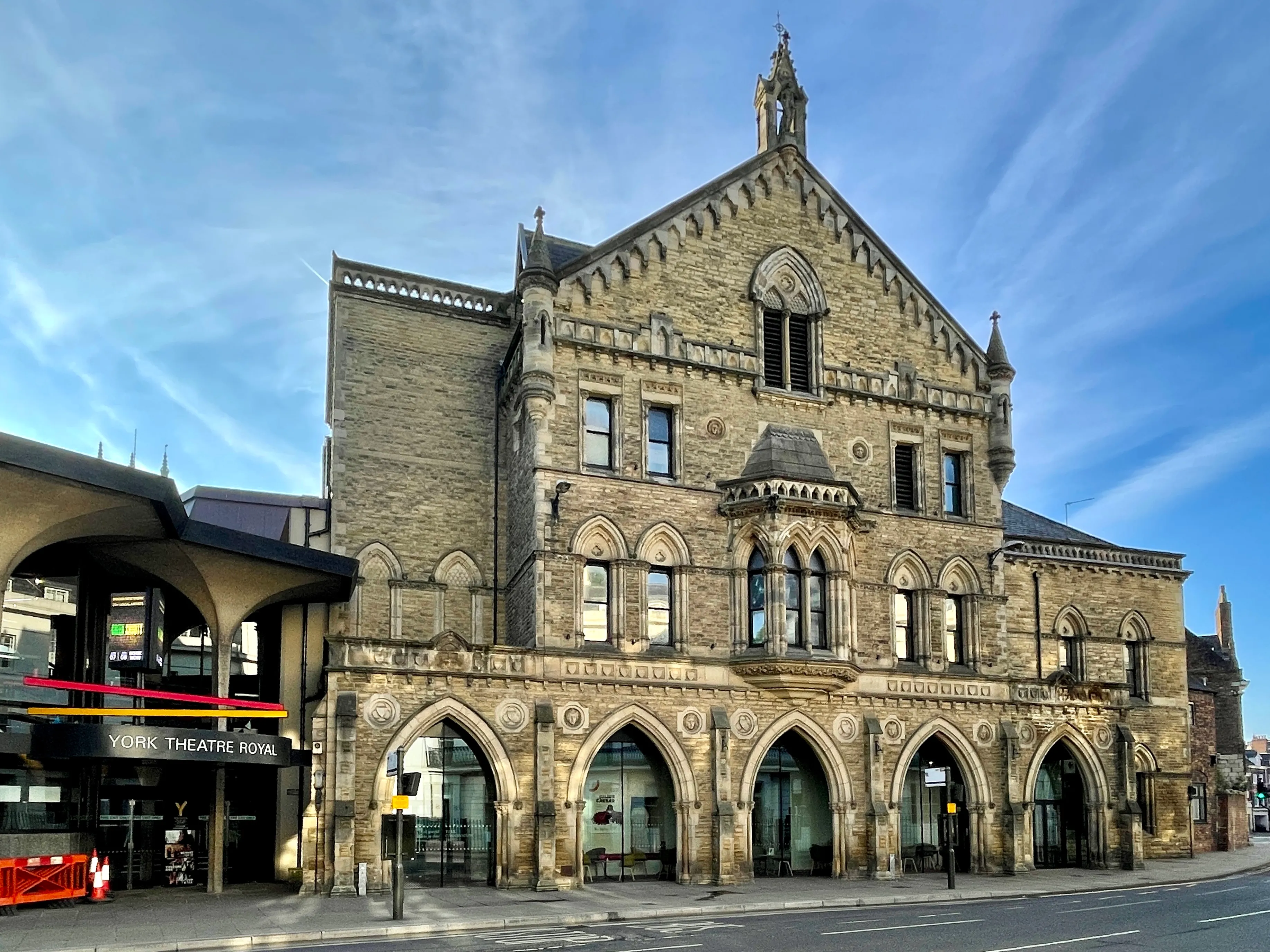 Fachada de piedra del York Theatre Royal que presenta ventanas y entradas con arcos góticos bajo un cielo azul.