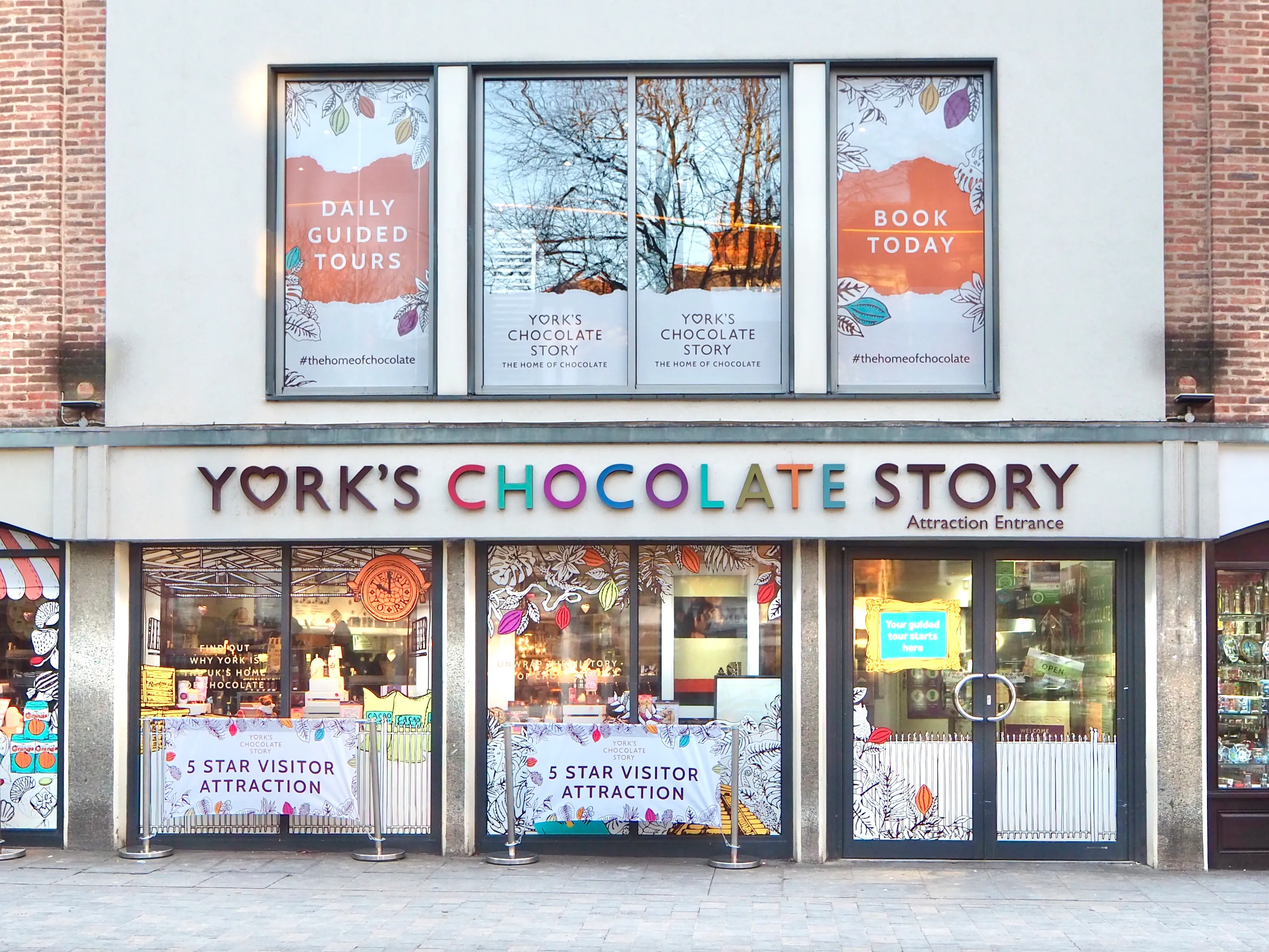 Fachada exterior de la entrada de la atracción York's Chocolate Story con grandes carteles coloridos, escaparates y pósteres promocionales.