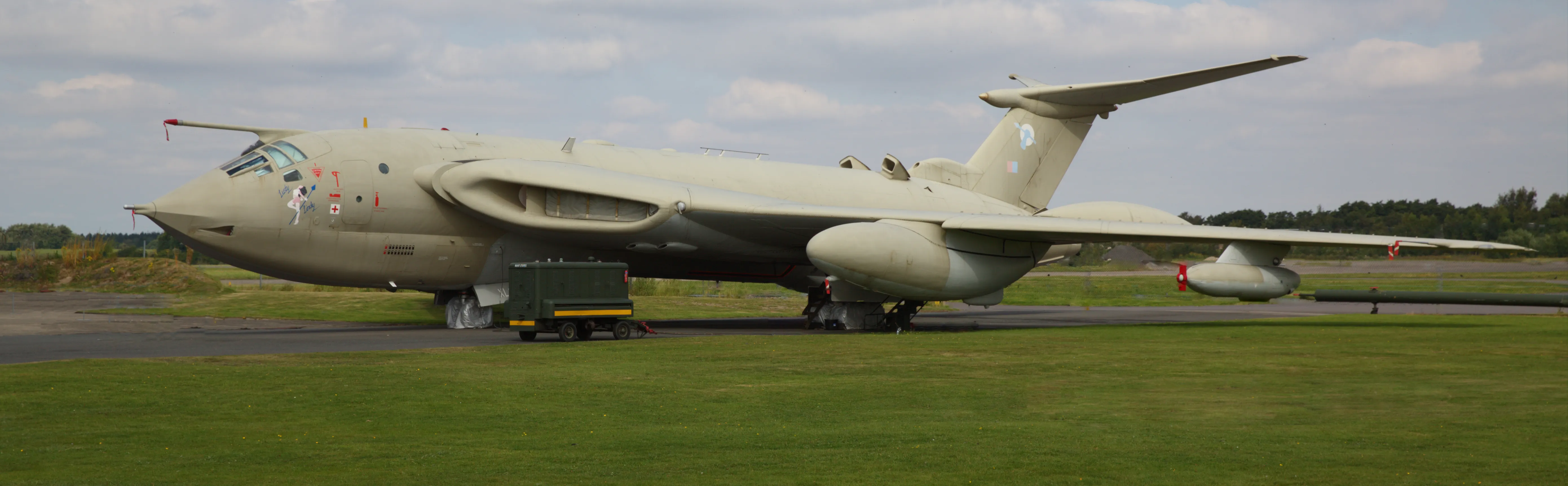 Een groot lichtgrijs militair vliegtuig van het type Handley-Page Victor K.2 dat op een tarmac geparkeerd staat, met groen gras op de voorgrond onder een bewolkte lucht.