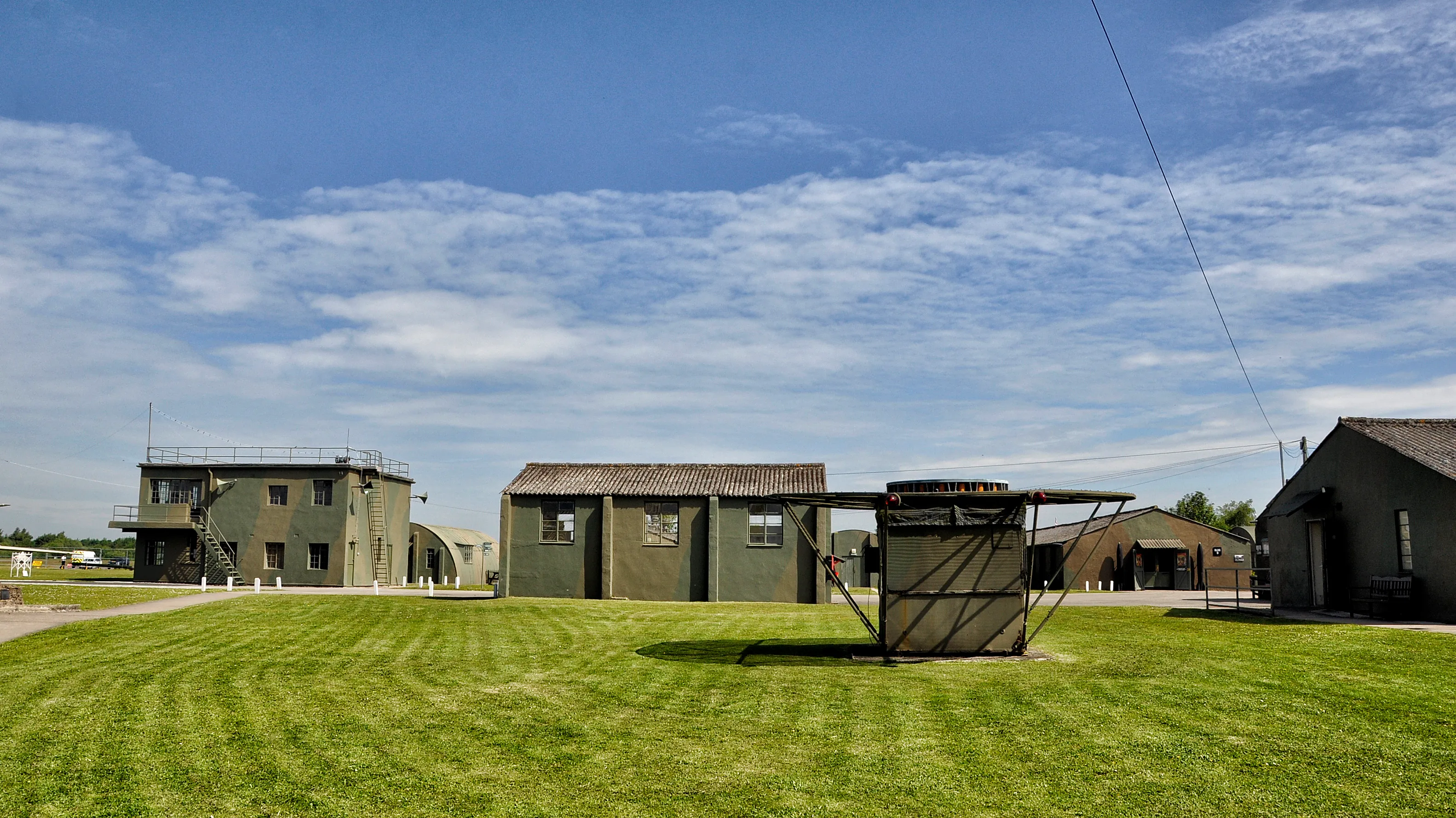 Historische militaire gebouwen en een verkeerstoren op een grasveld bij het Yorkshire Air Museum onder een blauwe lucht