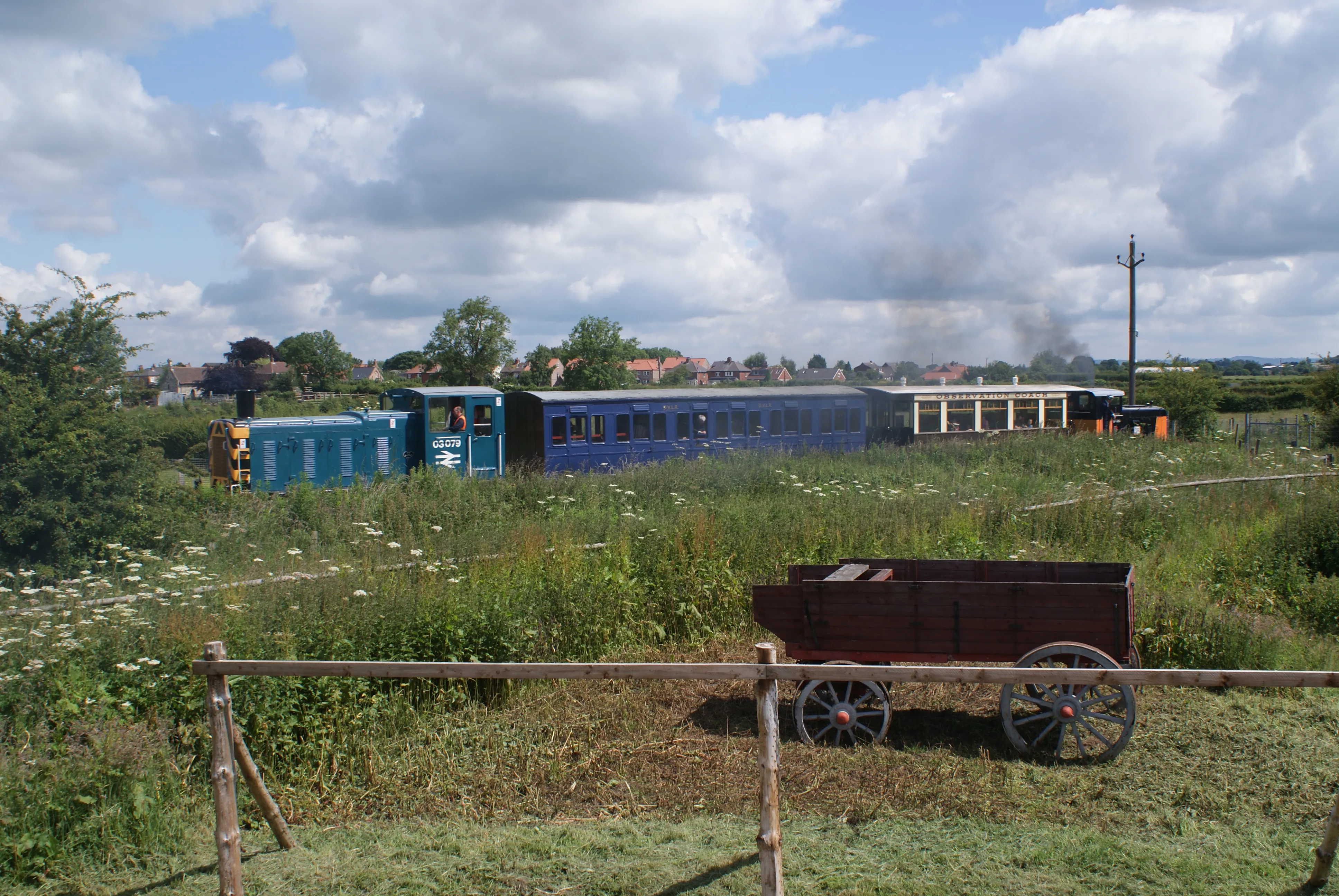Vagones de tren azules y un carro de madera en un campo de hierba bajo un cielo nublado en el Yorkshire Museum of Farming.