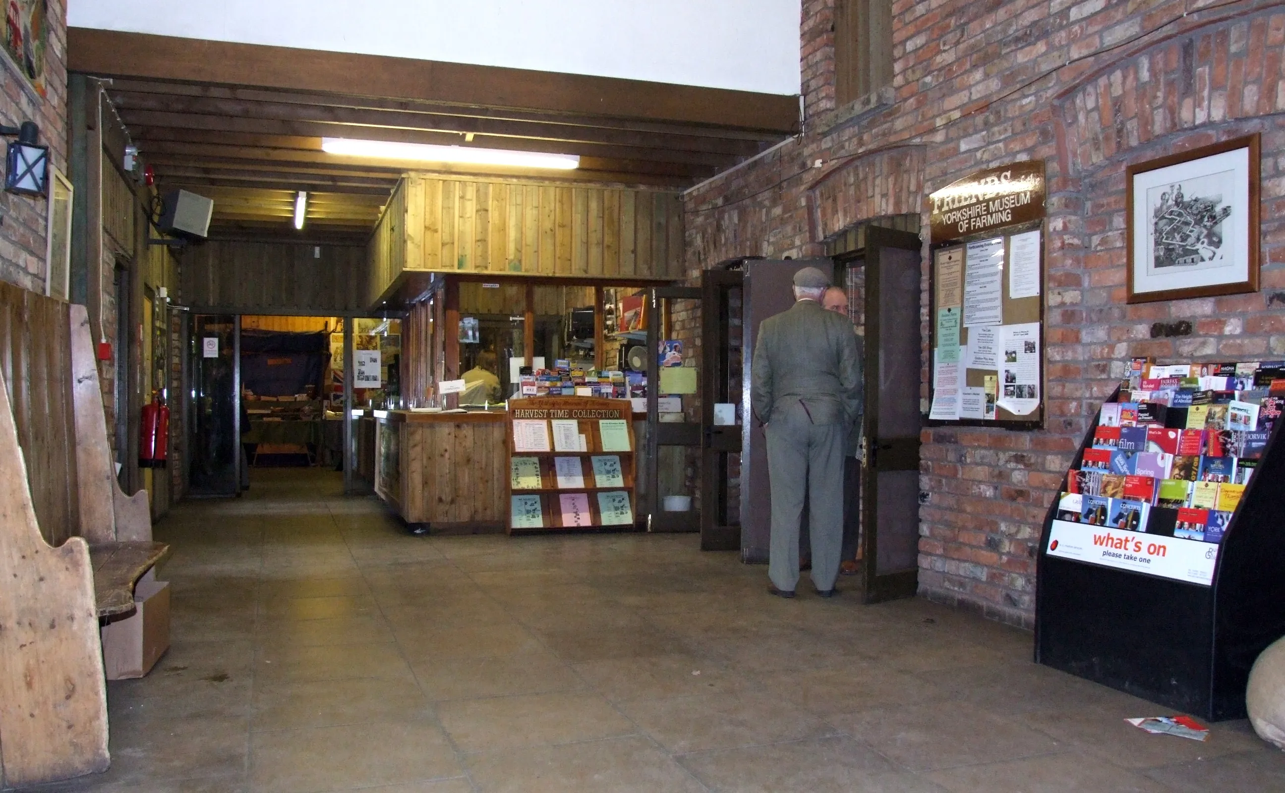 Binnenkomst van het Yorkshire Museum of Farming met bakstenen muren, een houten winkelbalie, een etalagepop in uniform en een display met boeken en brochures.