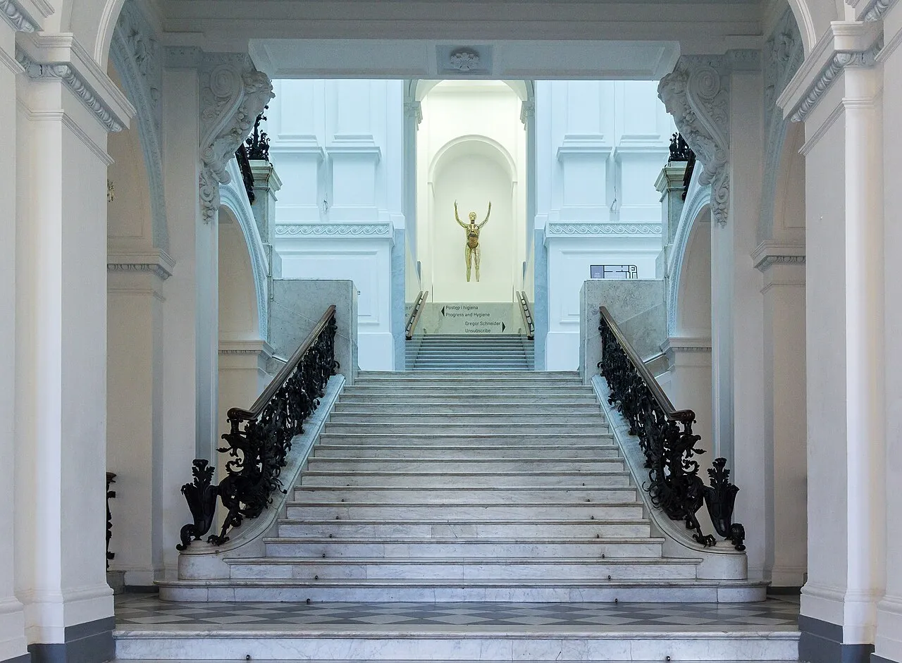 Gran escalera con barandillas negras ornamentadas y una escultura dorada en la parte superior