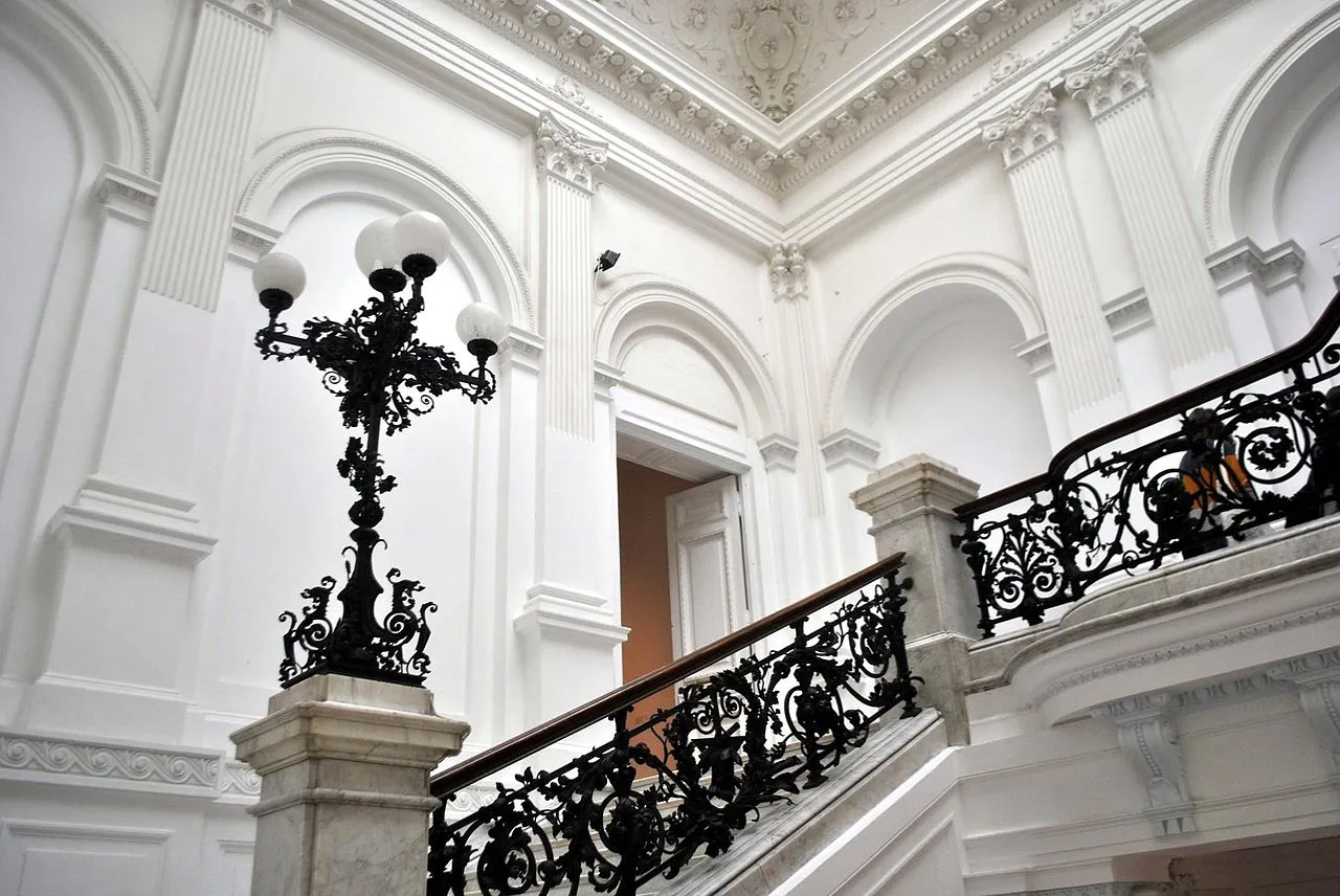 Barandilla de escalera y farola de hierro negro ornamentado en un espacio interior blanco y clásico