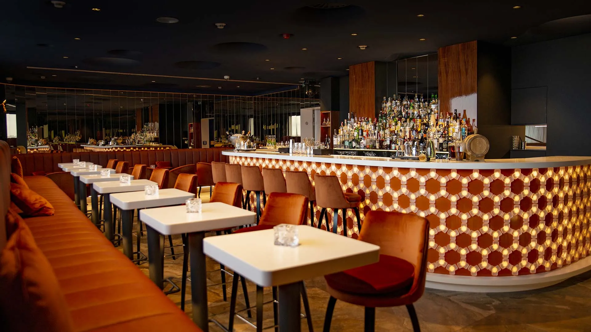 Interior de un restaurante con mesas modernas, sillas rojas y una barra con patrón hexagonal e iluminación