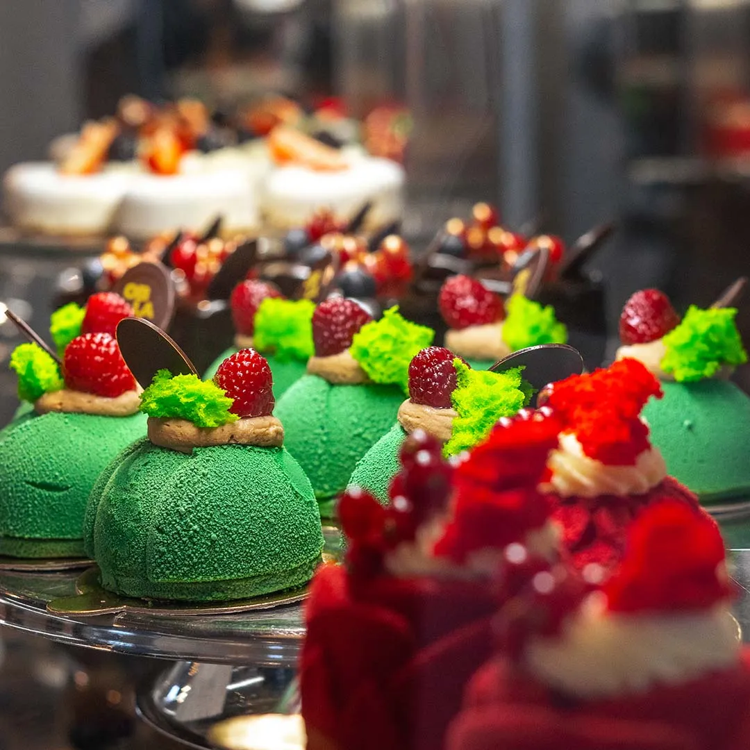 variedad de pasteles coloridos con coberturas verdes y rojas en exhibición en una vitrina de cristal