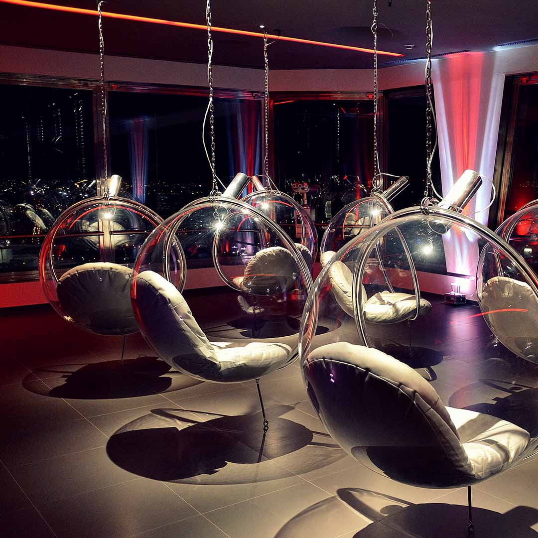 sillas esféricas con cojines blancos suspendidas del techo en una sala tenuemente iluminada con luces rojas y azules