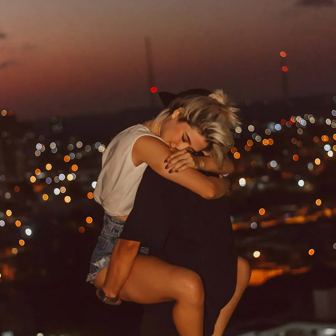 Dos personas abrazándose con un paisaje urbano al atardecer de fondo