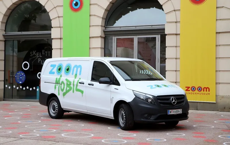 Furgoneta blanca con grafitis de 'zoom MOBIL' aparcada delante de un edificio con marca 'zoom' colorida y ventanas arqueadas